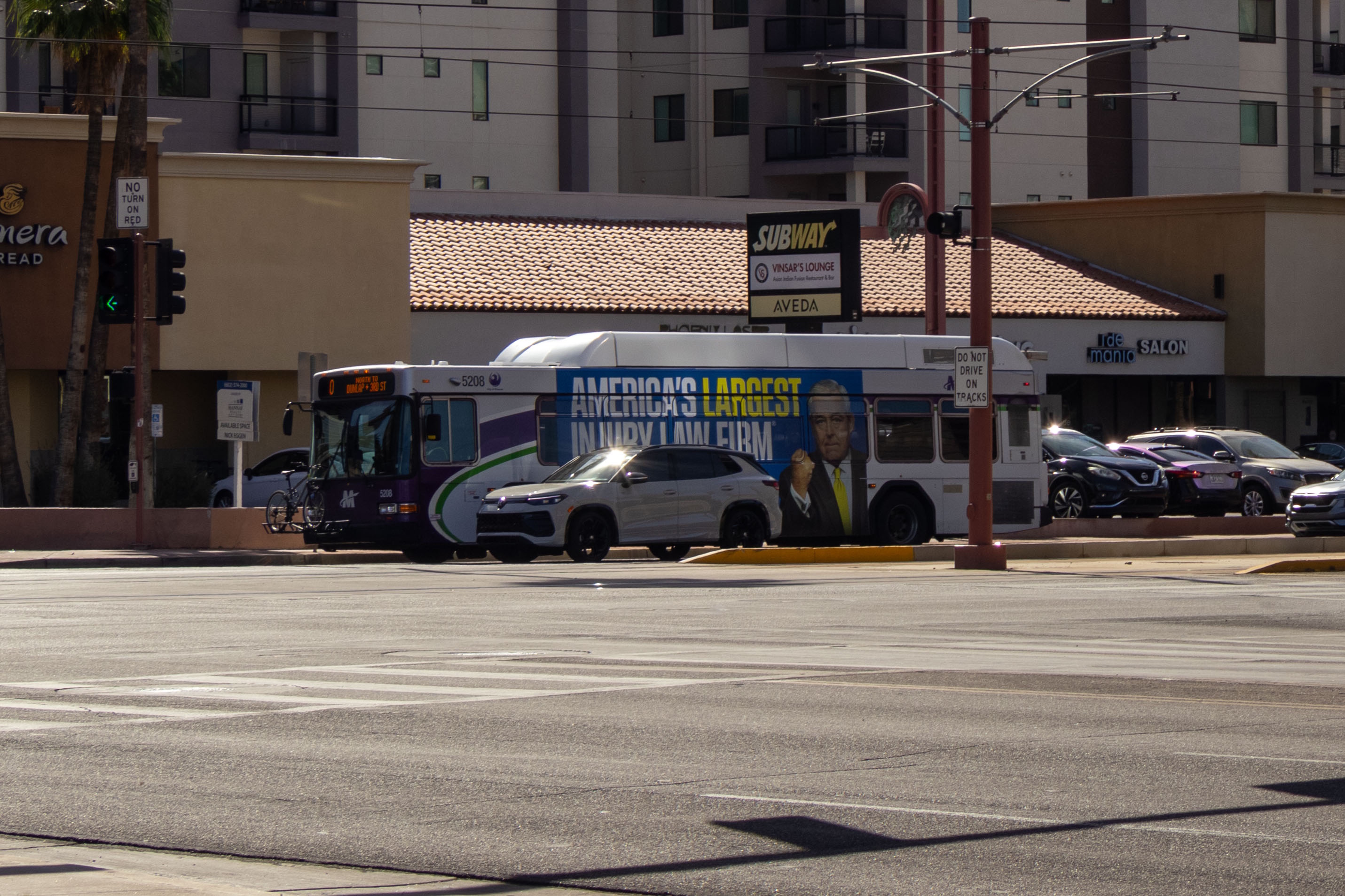 A white and gray Valley Metro bus, with purple and green accent colors, number 5208, traveling northbound on Central Avenue in Phoenix on route 0 to Dunlap and 3rd Street