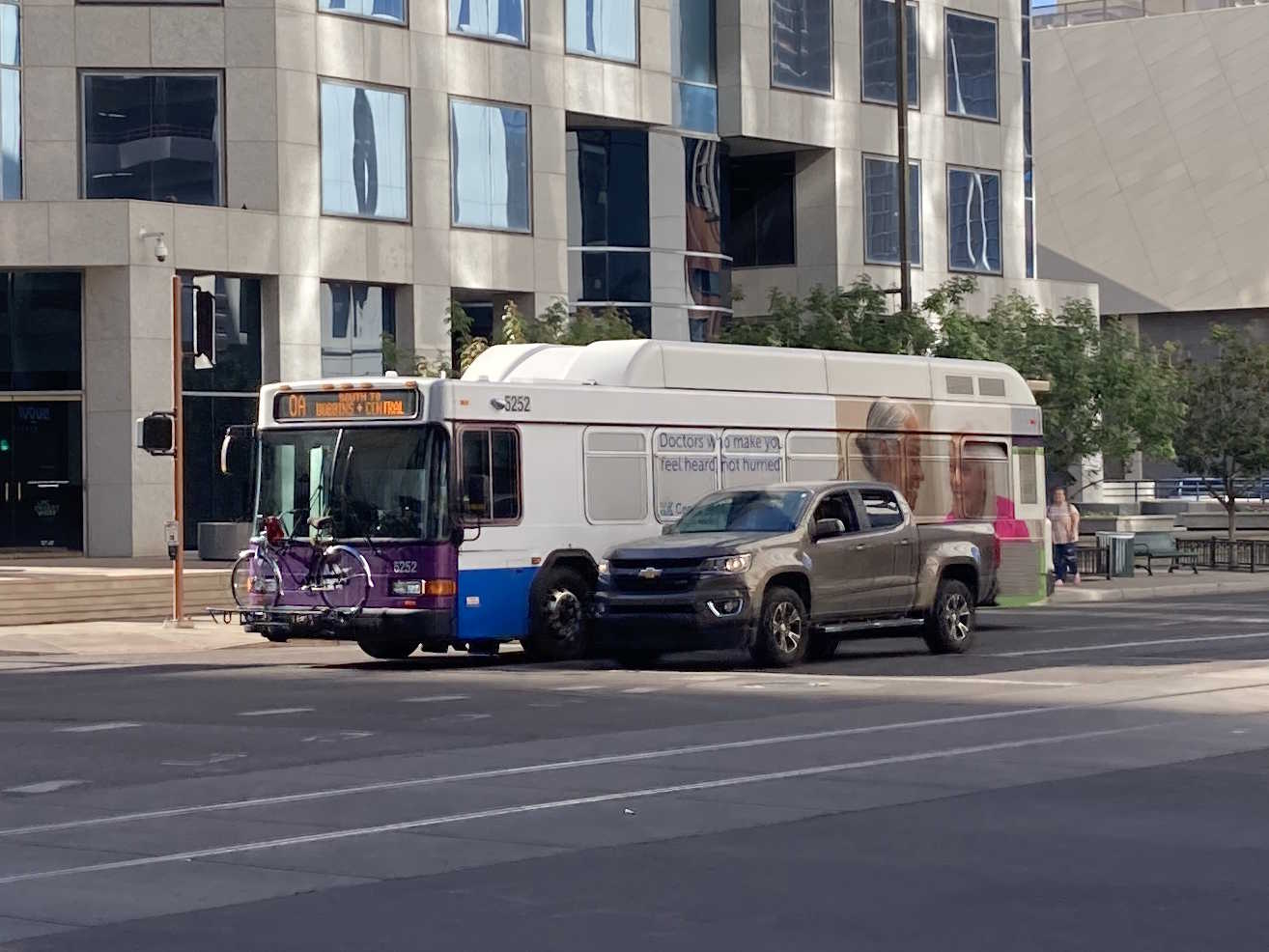 A white and gray Valley Metro bus, with purple and green accent colors, number 5252, traveling southbound on 1st Avenue in Phoenix on route 0A to Dobbins and Central