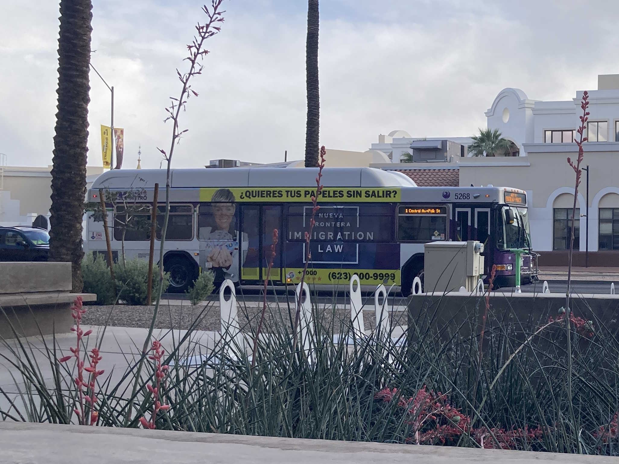 A white and gray Valley Metro bus, with purple and green accent colors, number 5268, traveling westbound on Van Buren Street in Phoenix on route 1 to Central Avenue and Polk Street