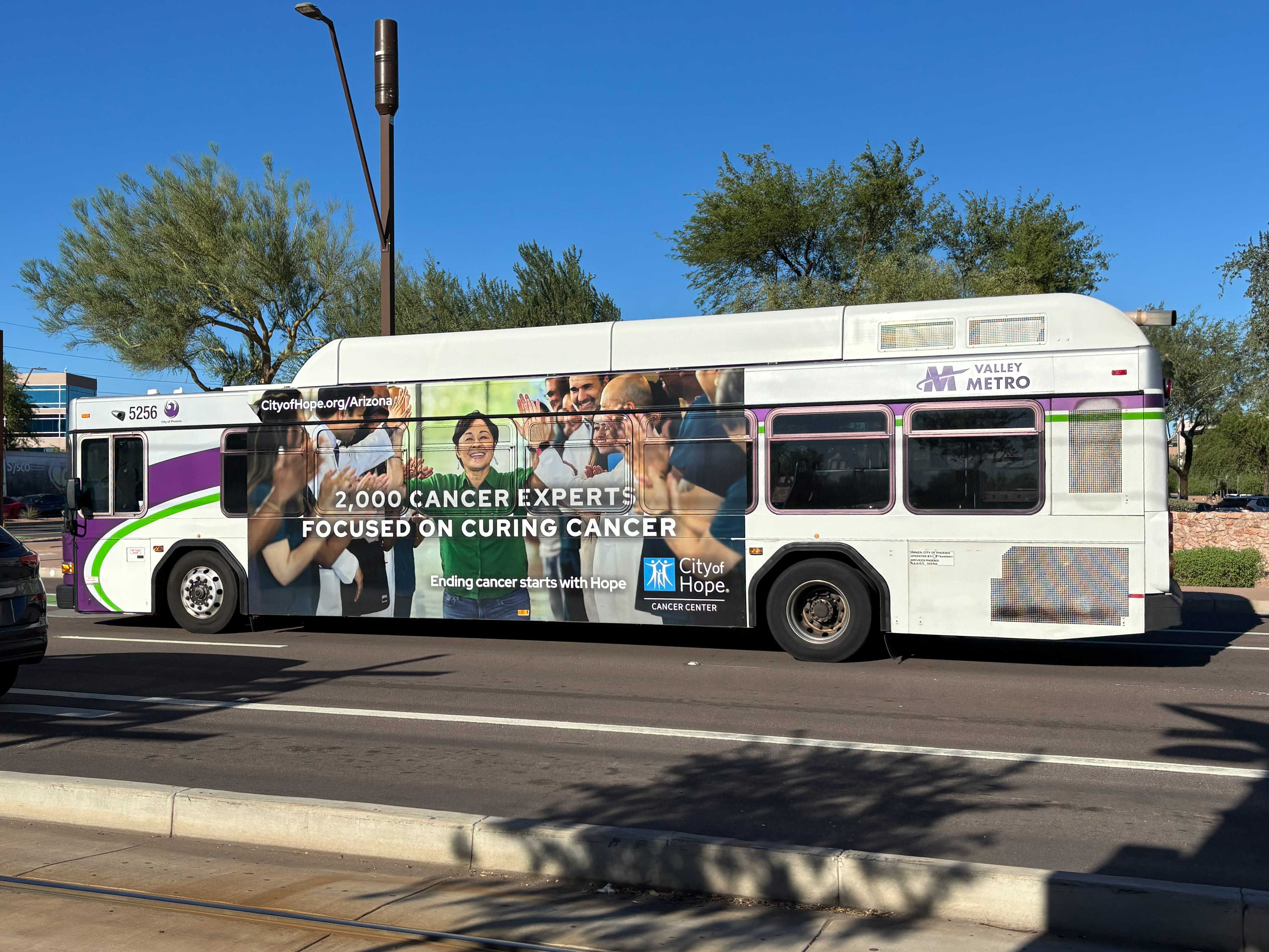 A white and gray Valley Metro bus, with purple and green accent colors, number 5256, traveling westbound on Washington Street in Tempe on route 1 to Greg Station Central Station