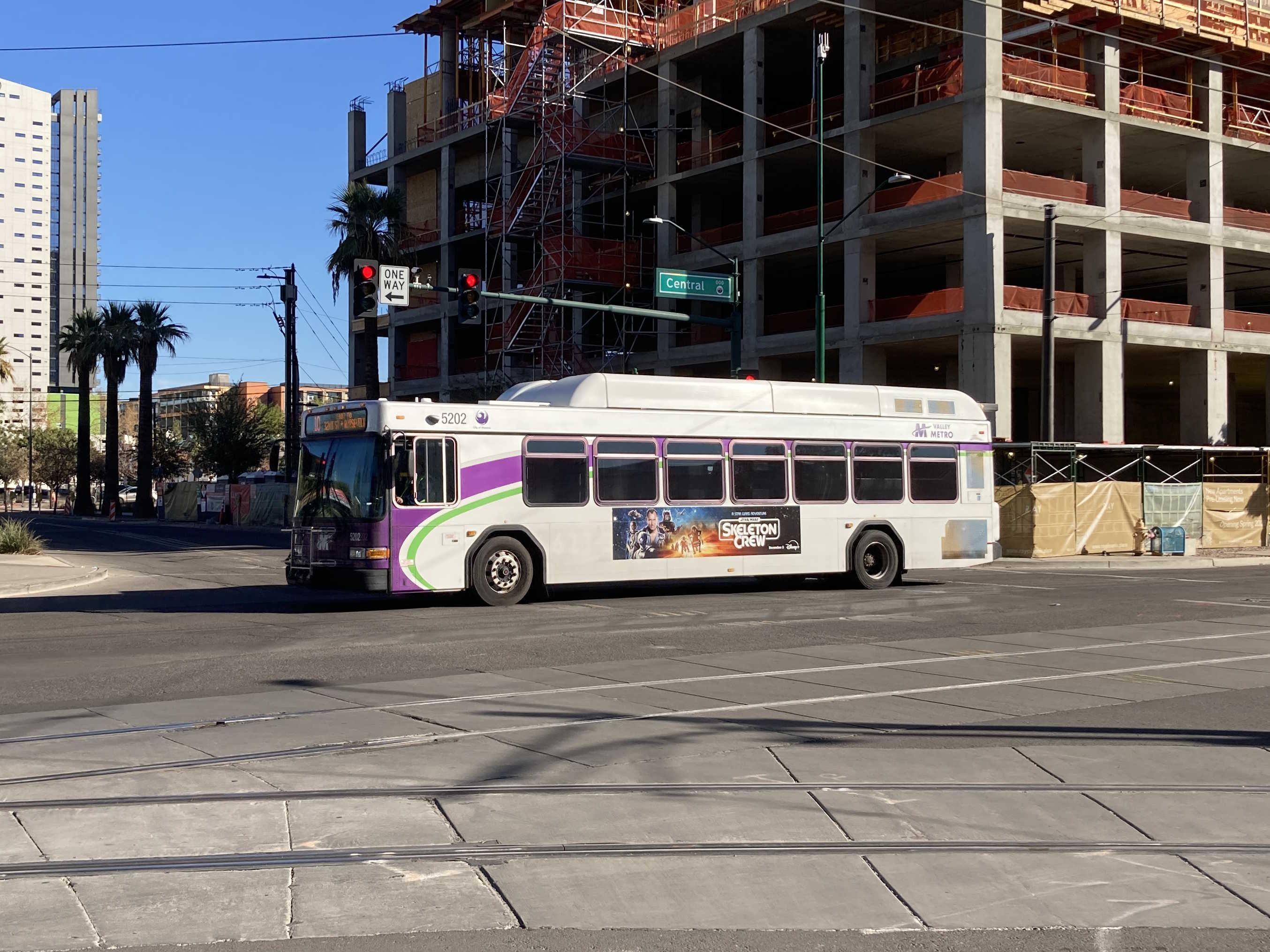 A white and gray Valley Metro bus, with purple and green accent colors, number 5202, traveling northbound on Central Avenue in Phoenix on route 10 to Roosevelt and 32nd Street