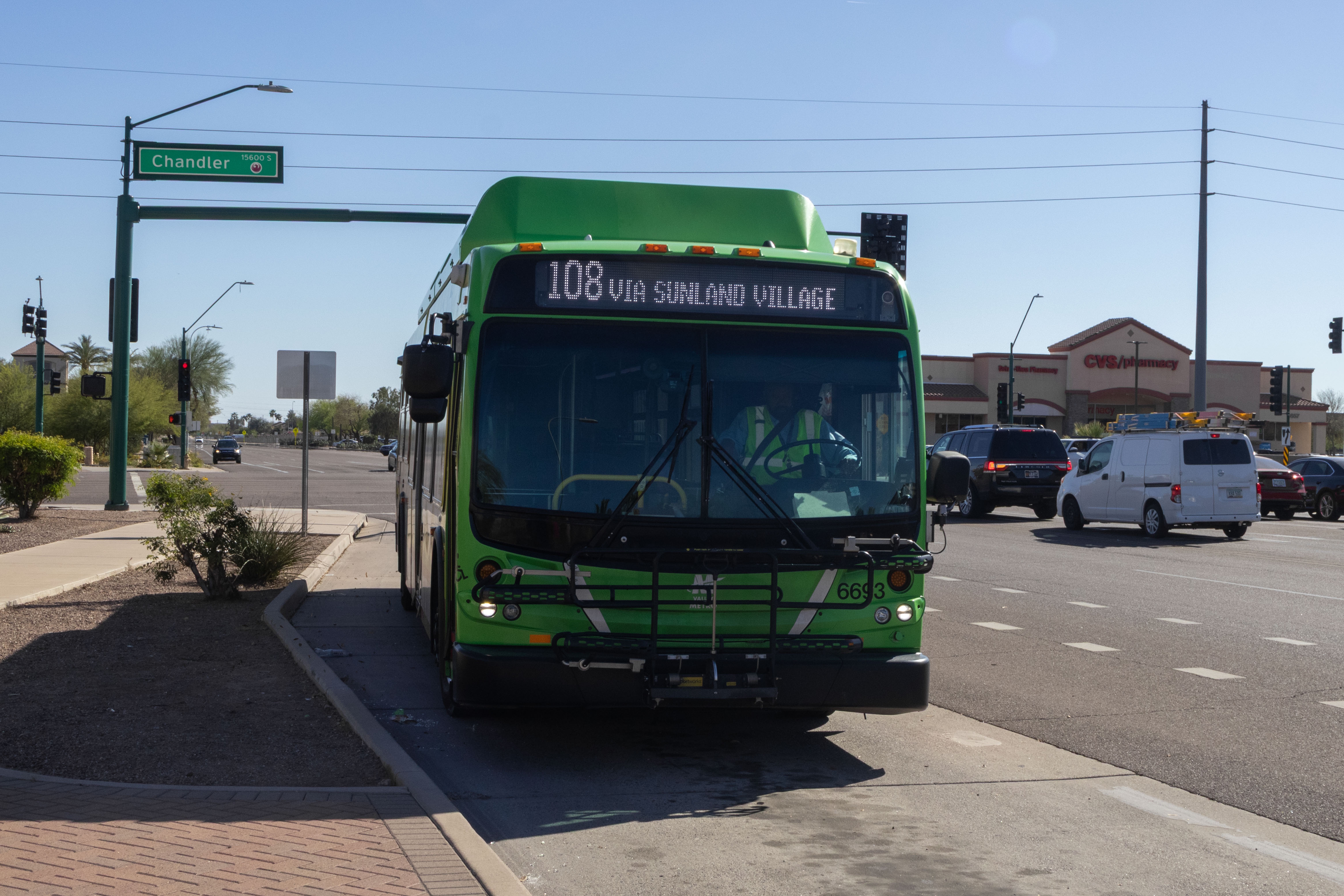A gray and green Valley Metro bus, with a purple and white stripe, number 6693, traveling northbound on 48th Street in Phoenix on route 108 to Superstition Springs Transit Center via Sunland Village