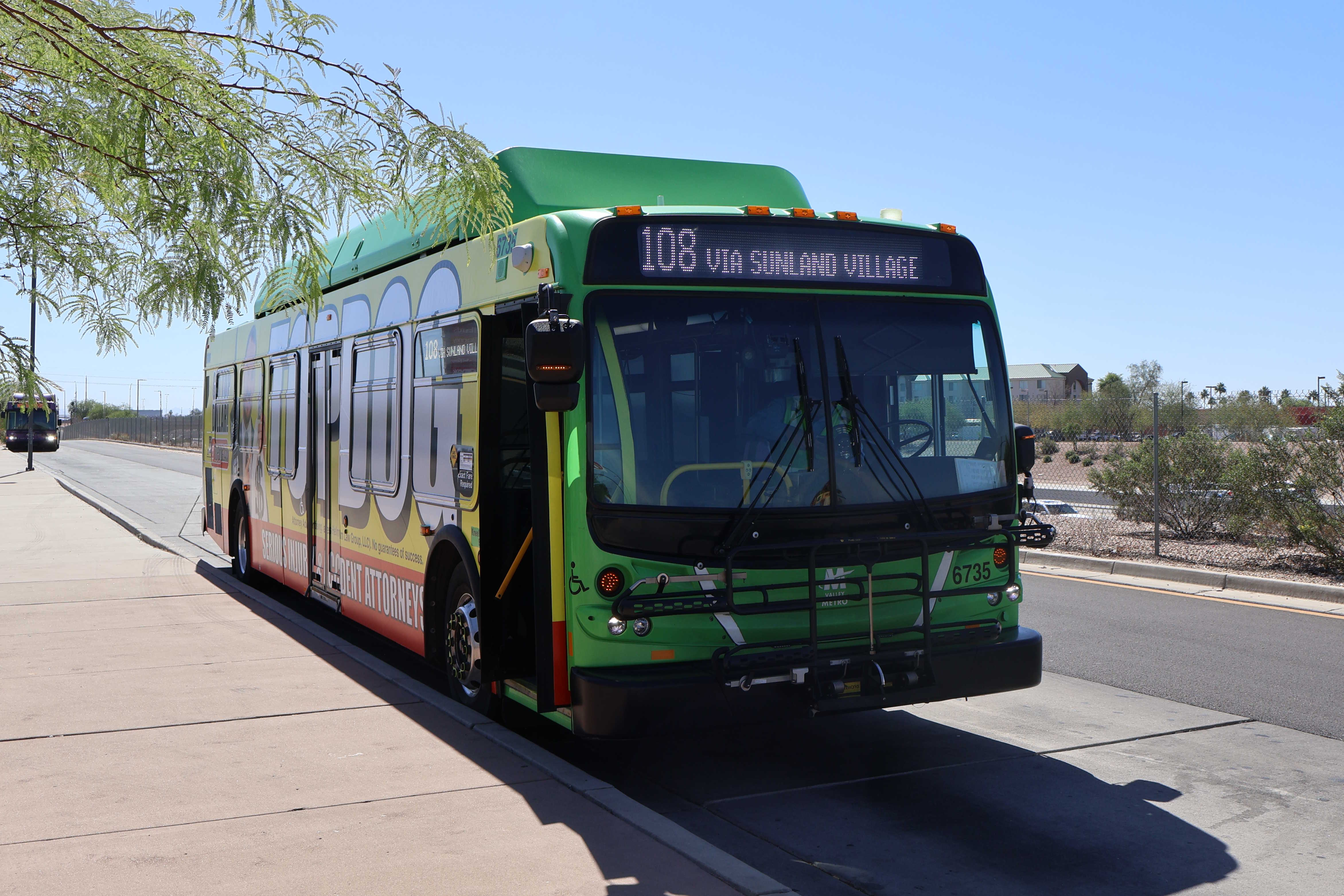 A gray and green Valley Metro bus, with a purple and white stripe, number 6735, at Superstition Springs Transit Center in Mesa on route 108 to 48th Street and Chandler Boulevard via Sunland Village
