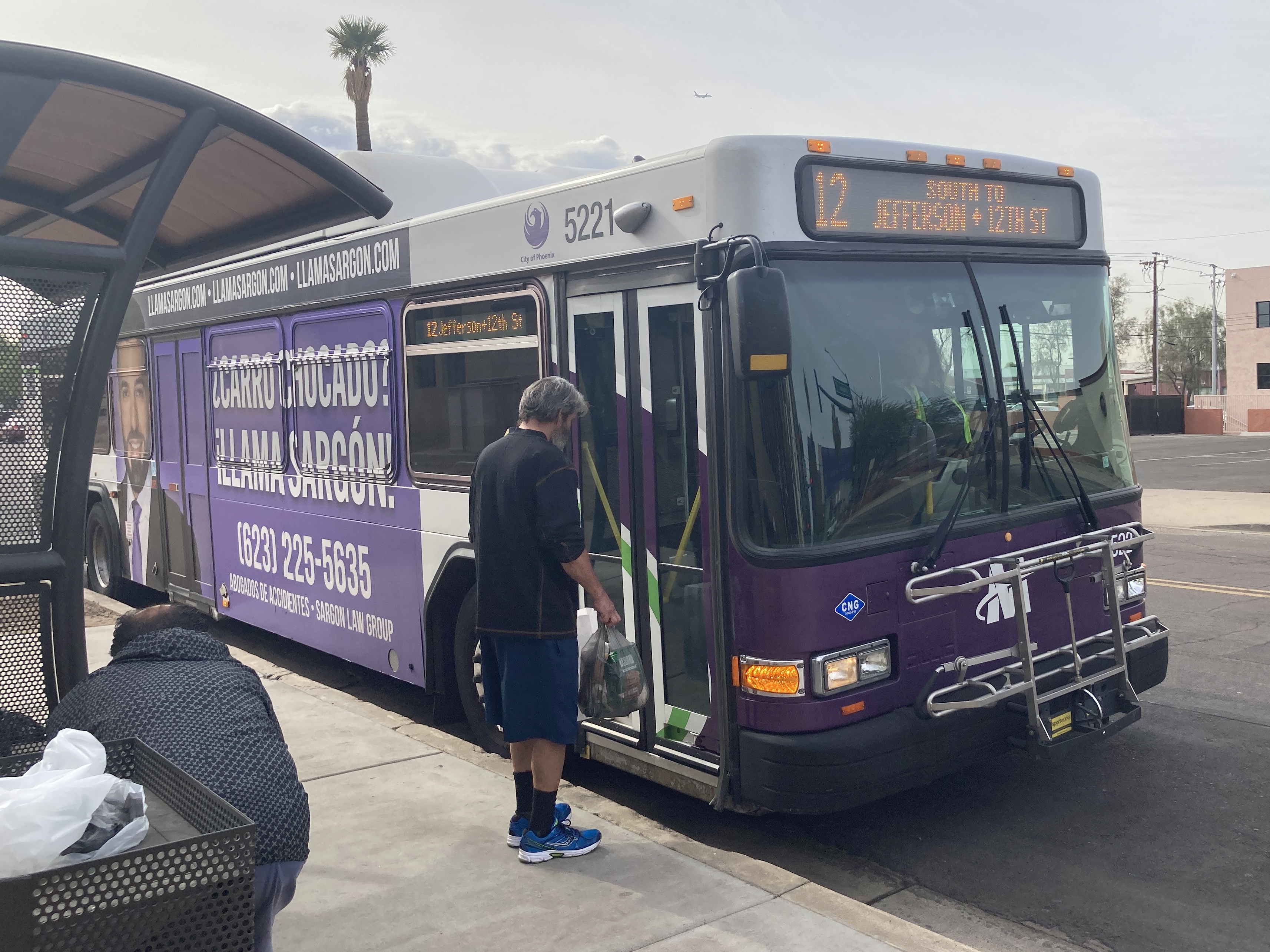 A white and gray Valley Metro bus, with purple and green accent colors, number 5221, traveling northbound on 12th Street in Phoenix on route 12 to 12th Street and Jefferson Street