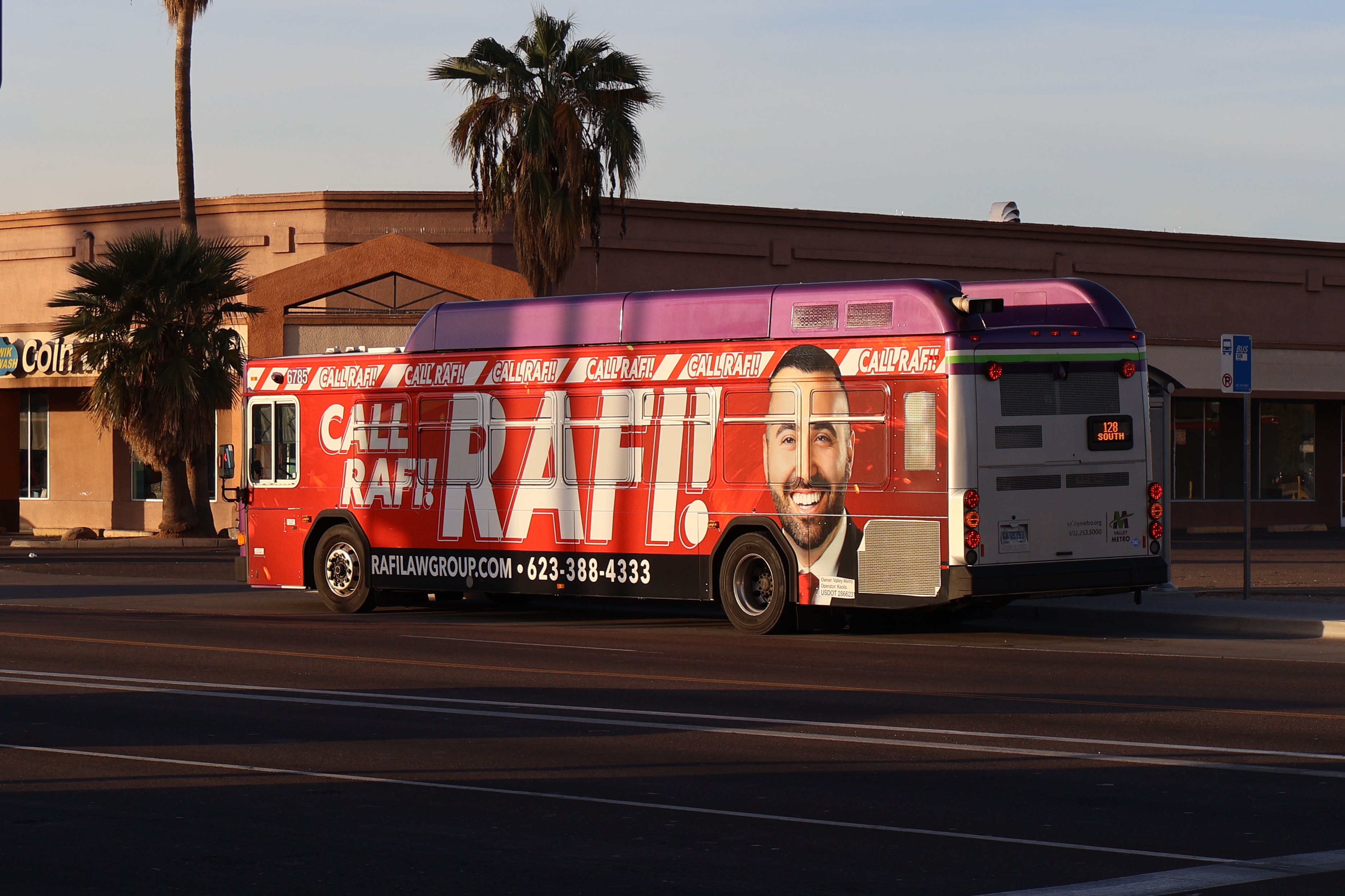 A gray and purple Valley Metro bus with a white and green stripe, number 6785, traveling southbound on Stapley Drive in Mesa on route 128 to Inverness Avenue and Stapley Drive