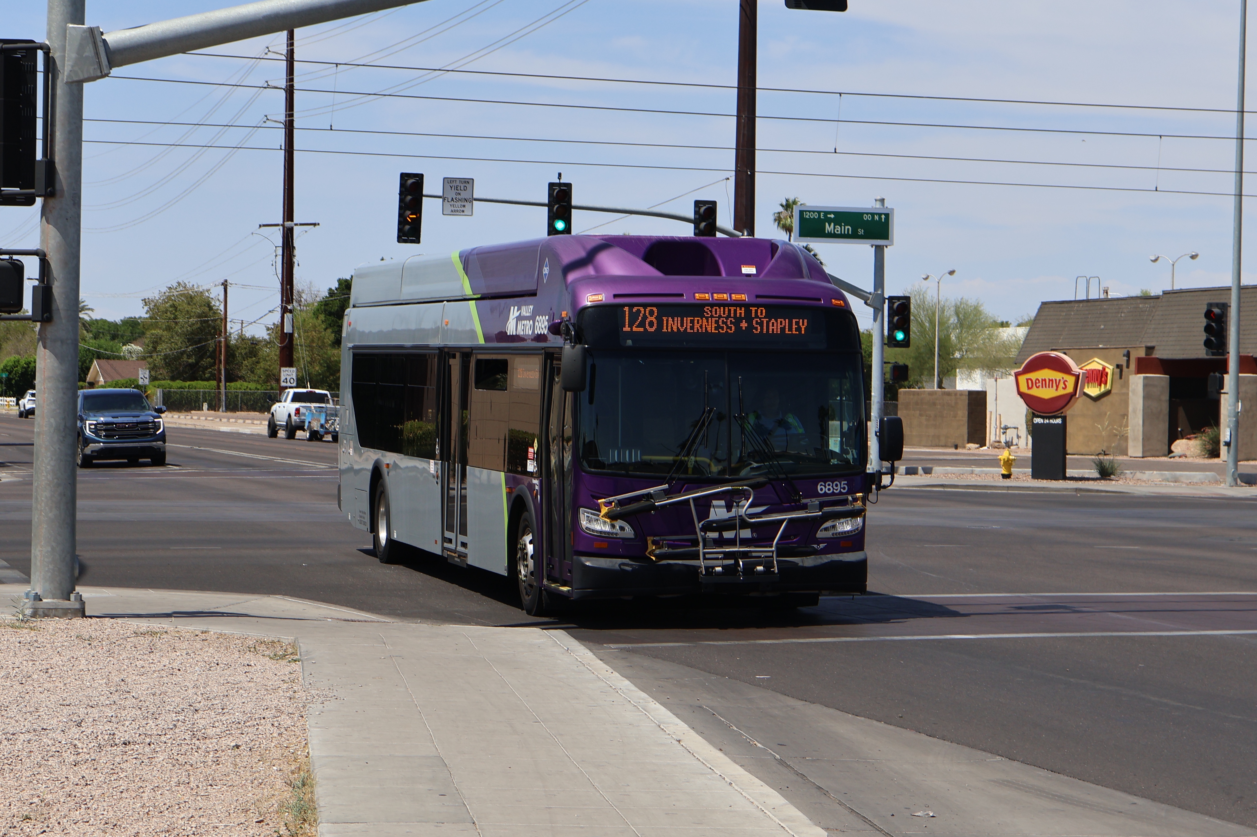 A gray and purple Valley Metro bus, with a green stripe, number 6895, traveling southbound on Stapley Drive in Mesa on route 128 to Inverness Avenue and Stapley Drive