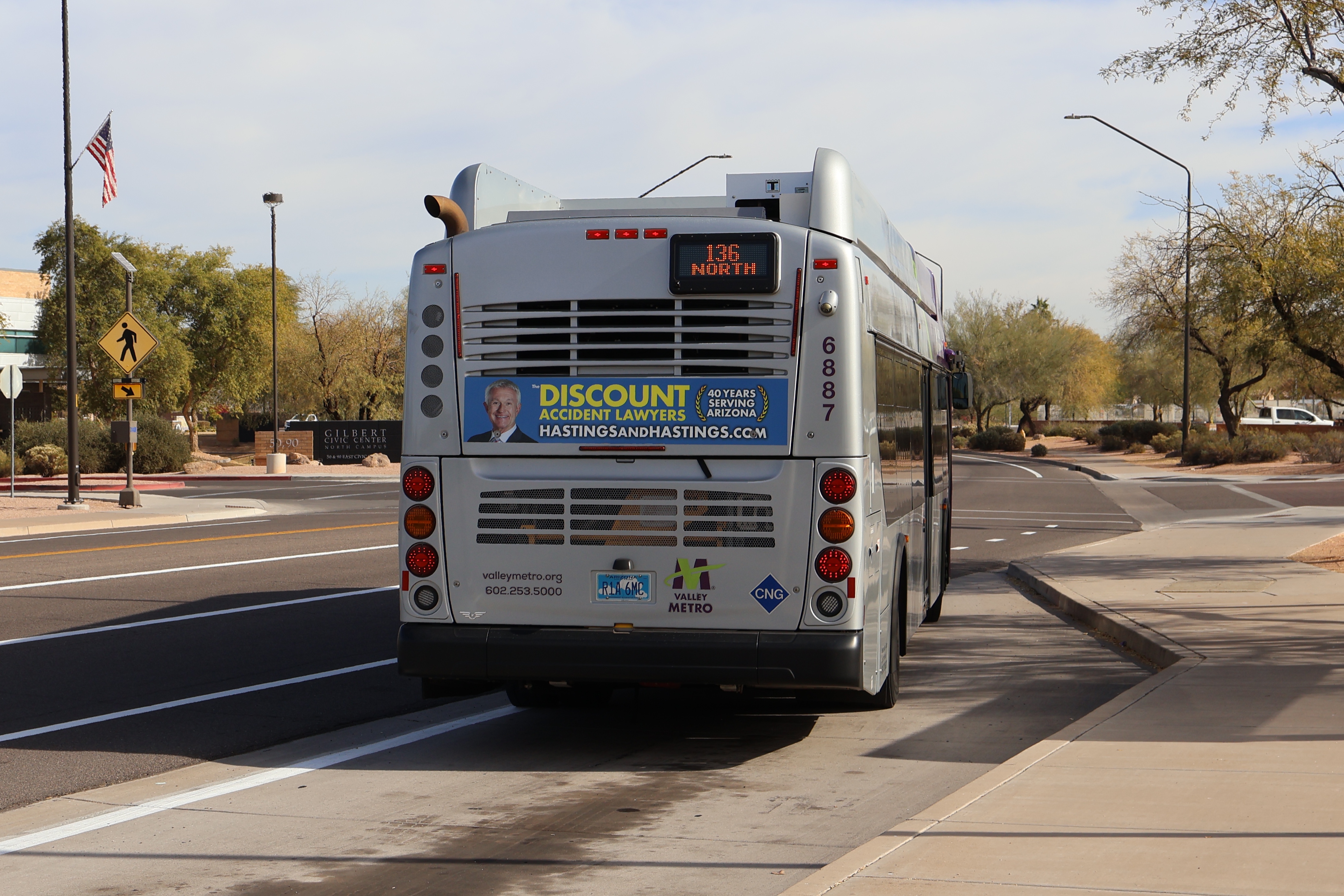 A gray and purple Valley Metro bus, with a green stripe, number 6887, traveling eastbound on Civic Center Drive in Gilbert on route 136 to Gilbert Road and McDowell Road