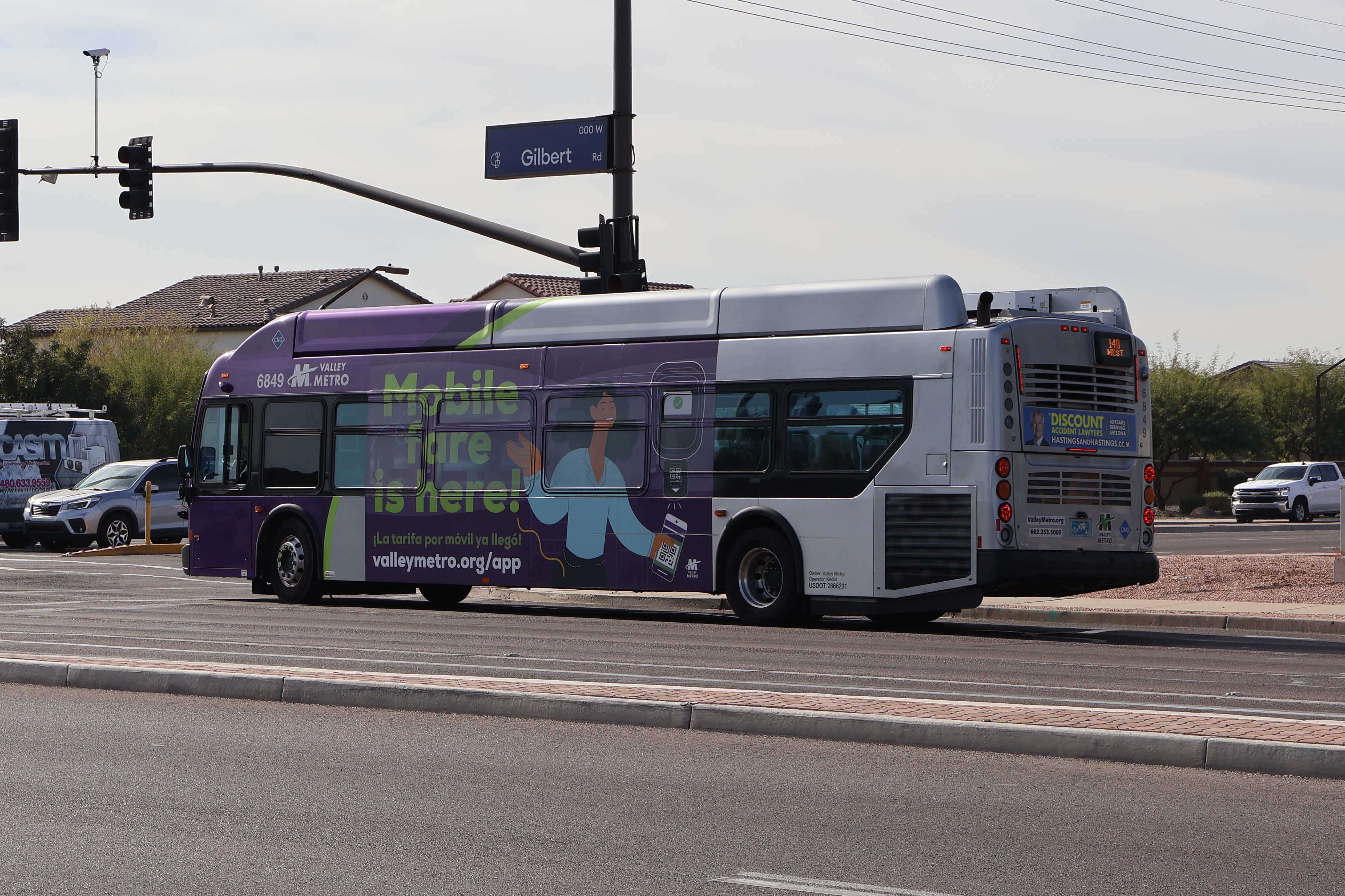 A gray and purple Valley Metro bus, with a green stripe, number 6849, traveling southbound on Gilbert Road in Gilbert on route 140 to Ray Road and 48th Street