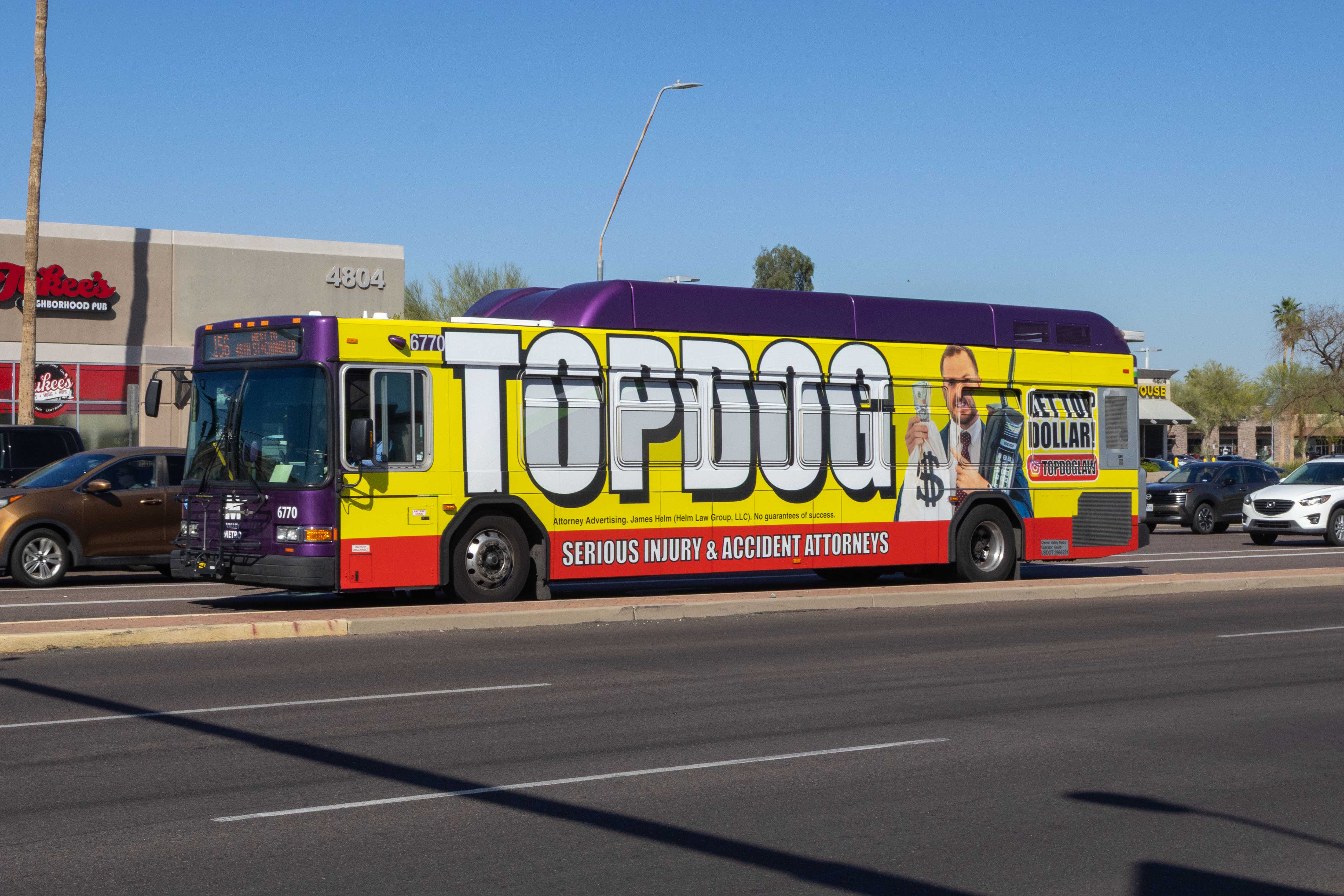 A gray and purple Valley Metro bus, with a green stripe, number 6770, traveling westbound on Chandler Boulevard in Phoenix on route 156 to 48th Street and Chandler Boulevard