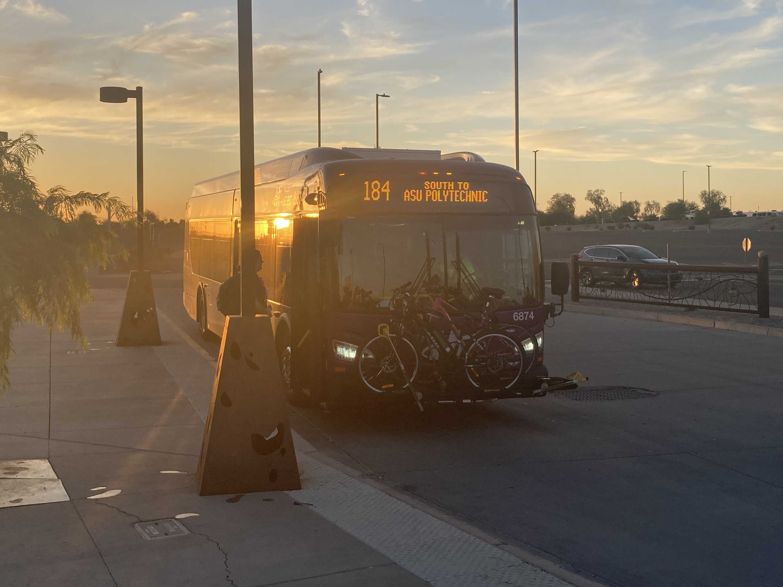 A gray and purple Valley Metro bus, with a green stripe, number 6874, at Superstition Springs Transit Center in Mesa on route 184 to Arizona State University Polytechnic