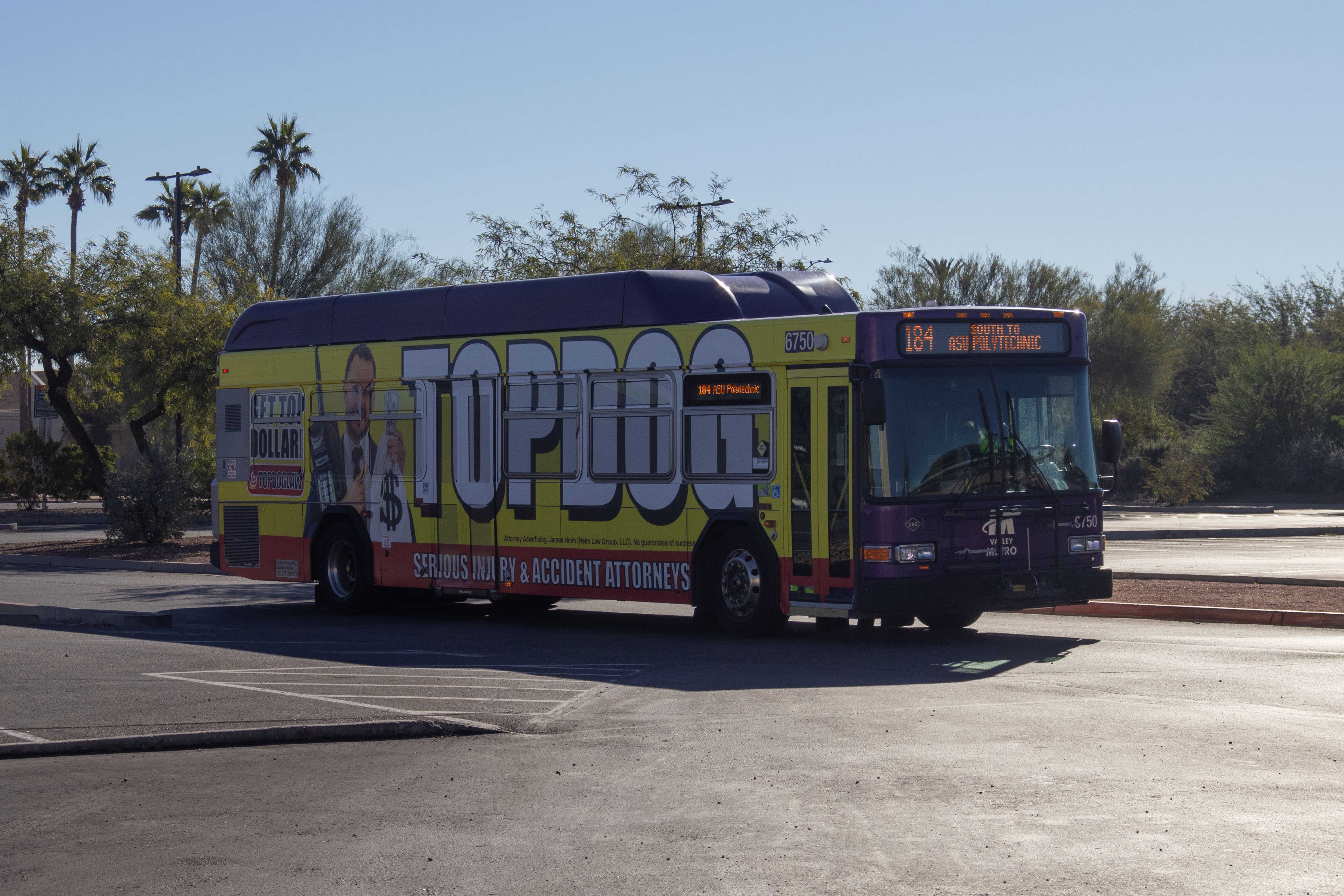 A gray and purple Valley Metro bus, with a white and green stripe, number 6750, traveling westbound on Tiburon Avenue in Mesa on route 184 to Arizona State University Polytechnic