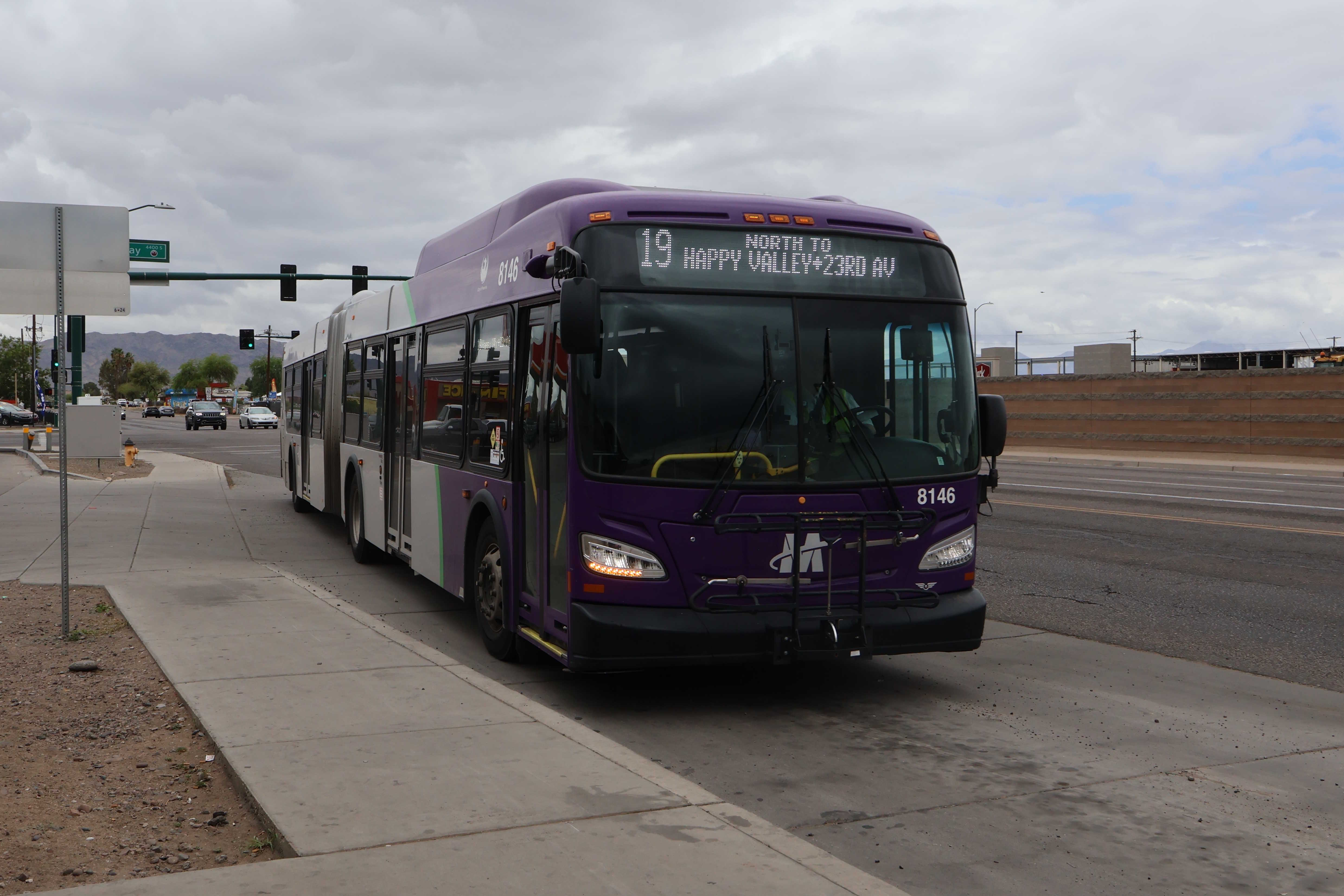 A purple and gray articulated Valley Metro bus, number 8146, traveling northbound on 19th Avenue in Phoenix on route 19 to 23rd Avenue and Happy Valley Road