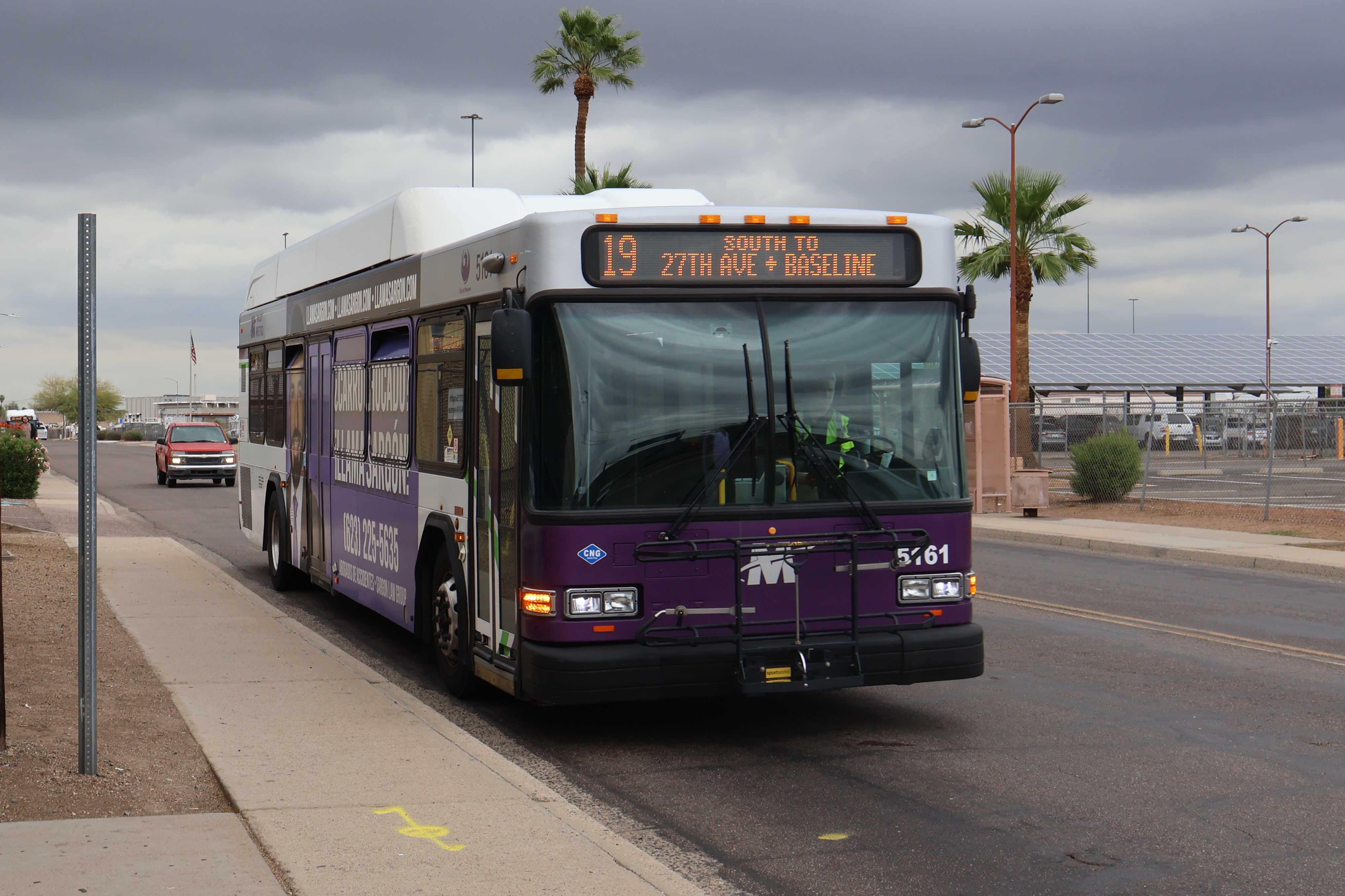 A white and gray Valley Metro bus, with purple and green accent colors, number 5161, traveling southbound on 22nd Avenue in Phoenix on route 19 to 27th Avenue and Baseline Road