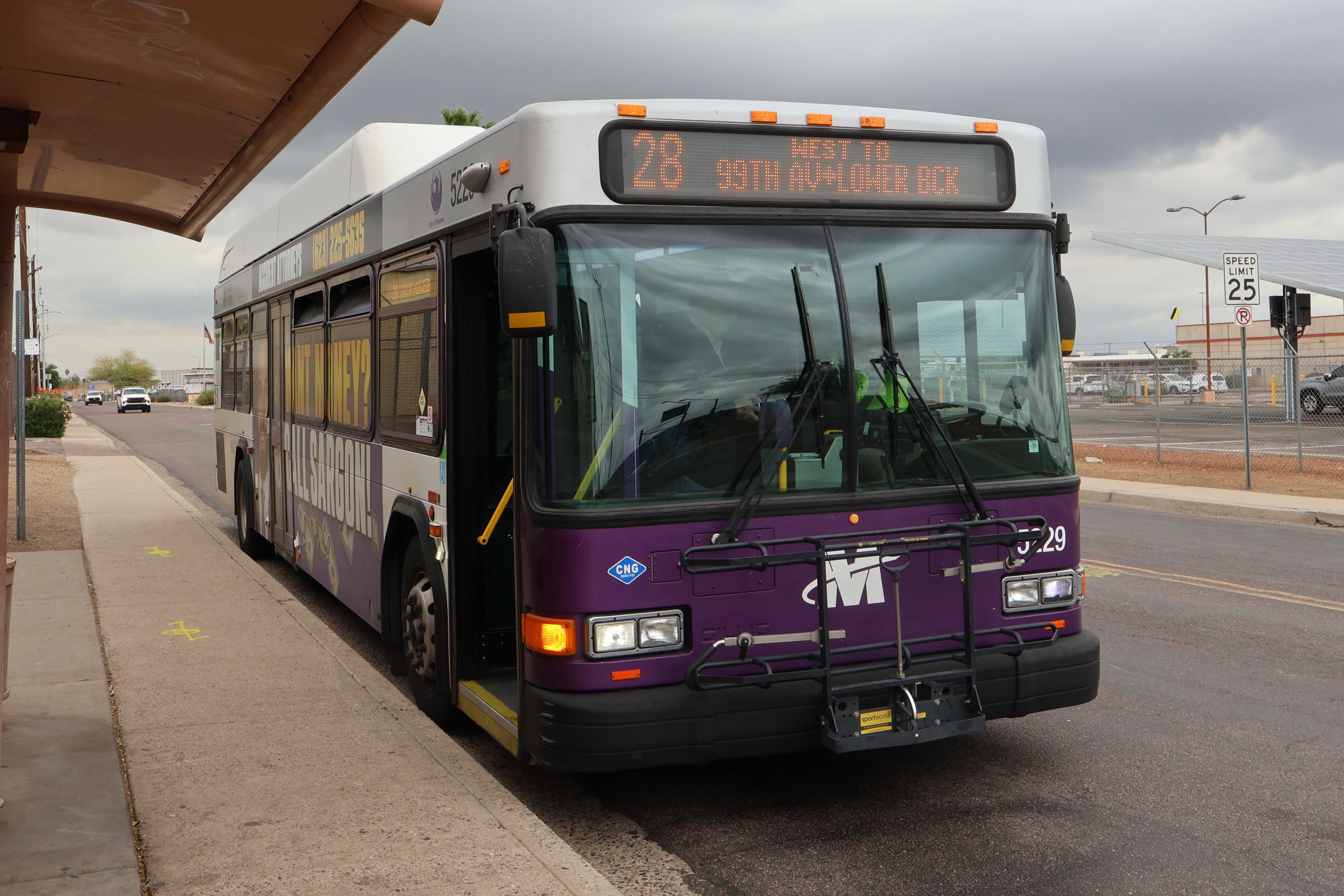A white and gray Valley Metro bus, with purple and green accent colors, number 5229, traveling southbound on 22nd Avenue in Phoenix on route 28 to Lower Buckeye Road and 99th Avenue