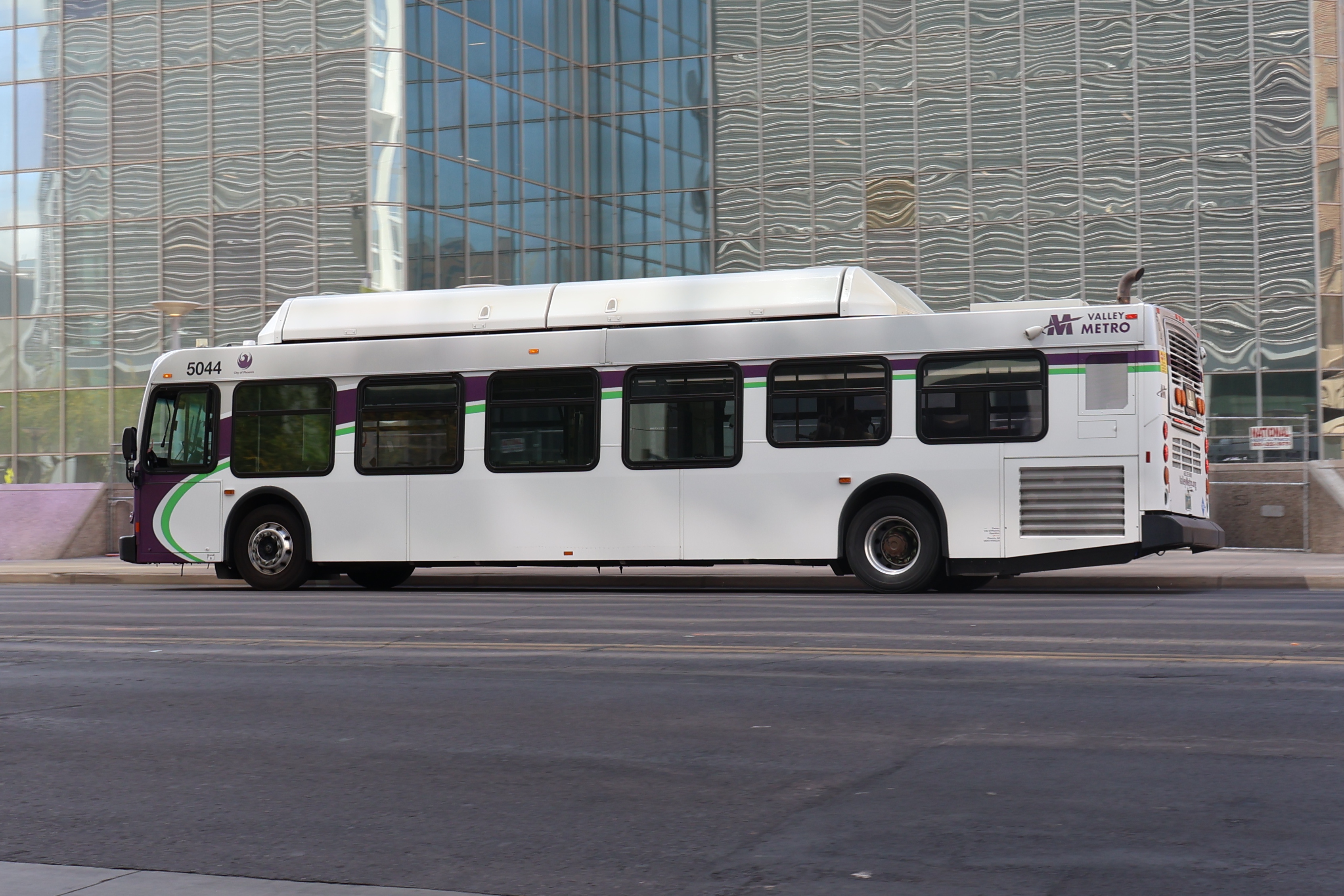 A white and gray Valley Metro bus, with purple and green accent colors, number 5044, traveling eastbound on Van Buren Street in Phoenix on route 3 to Phoenix Zoo