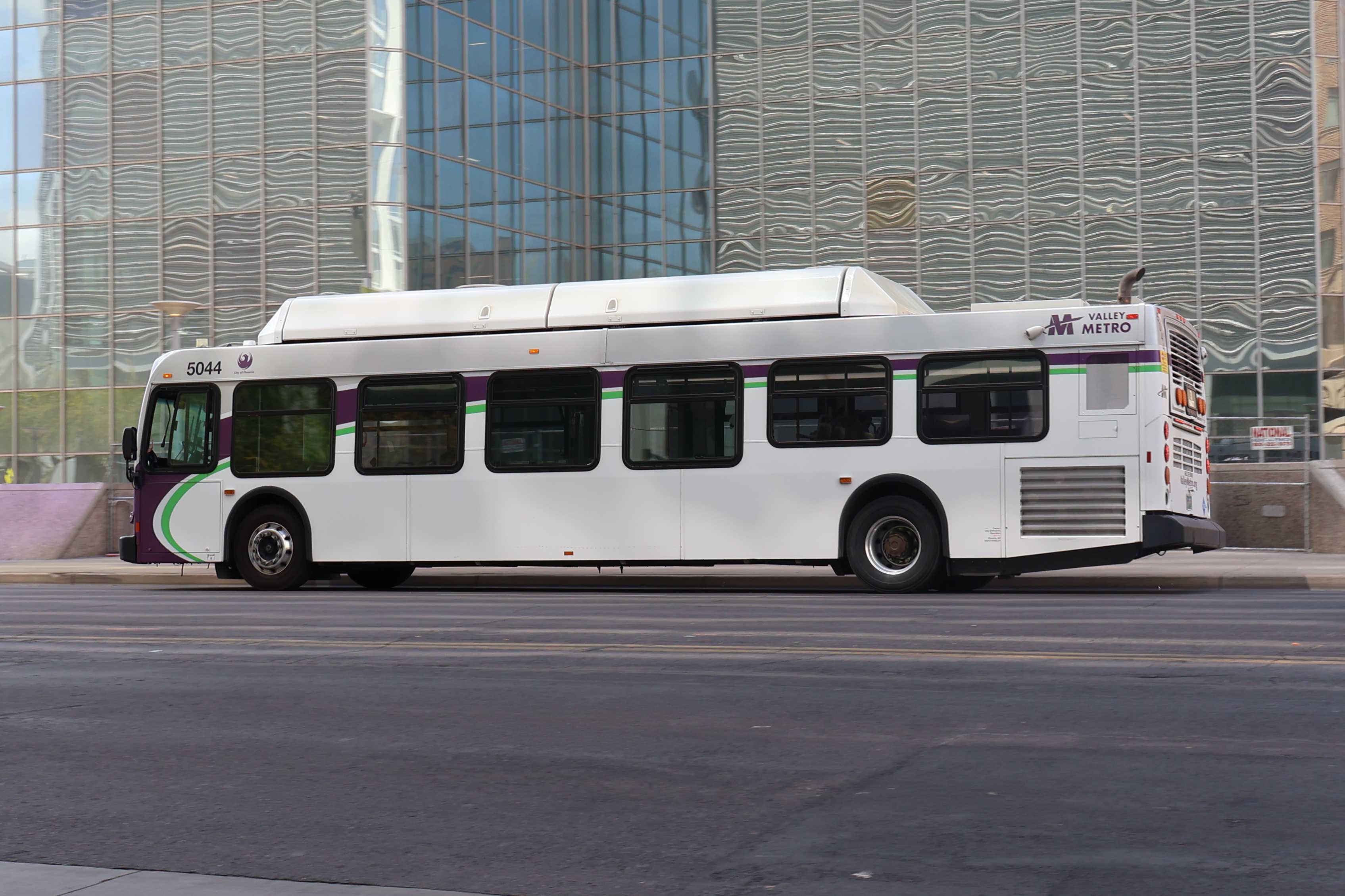 A white and gray Valley Metro bus, with purple and green accent colors, number 5044, traveling eastbound on Van Buren Street in Phoenix on route 3 to Phoenix Zoo