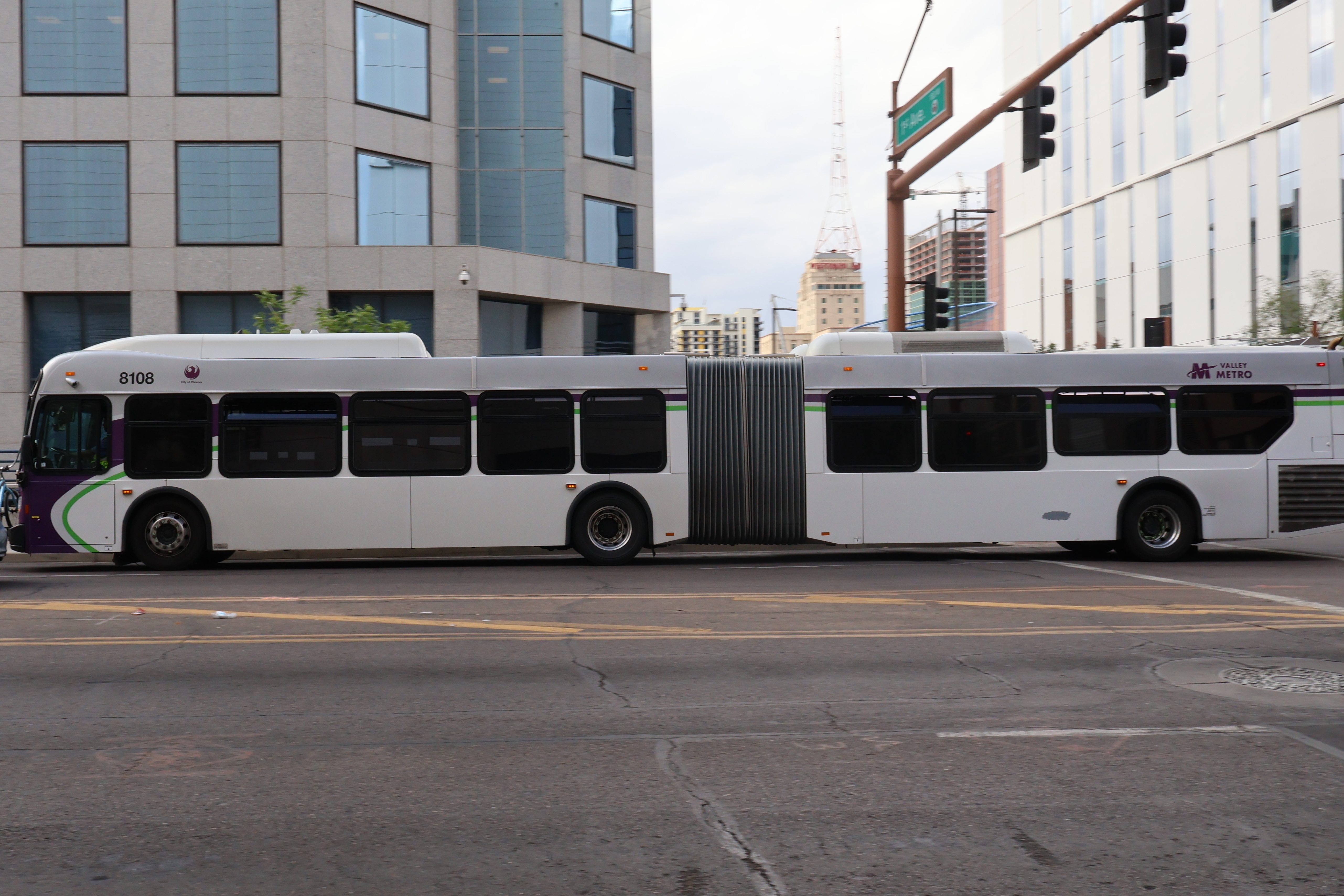 A white and gray articulated Valley Metro bus, with purple and green accent colors, number 8108, traveling westbound on Van Buren Street in Phoenix on route 3 to 4th Street and La Canada Boulevard