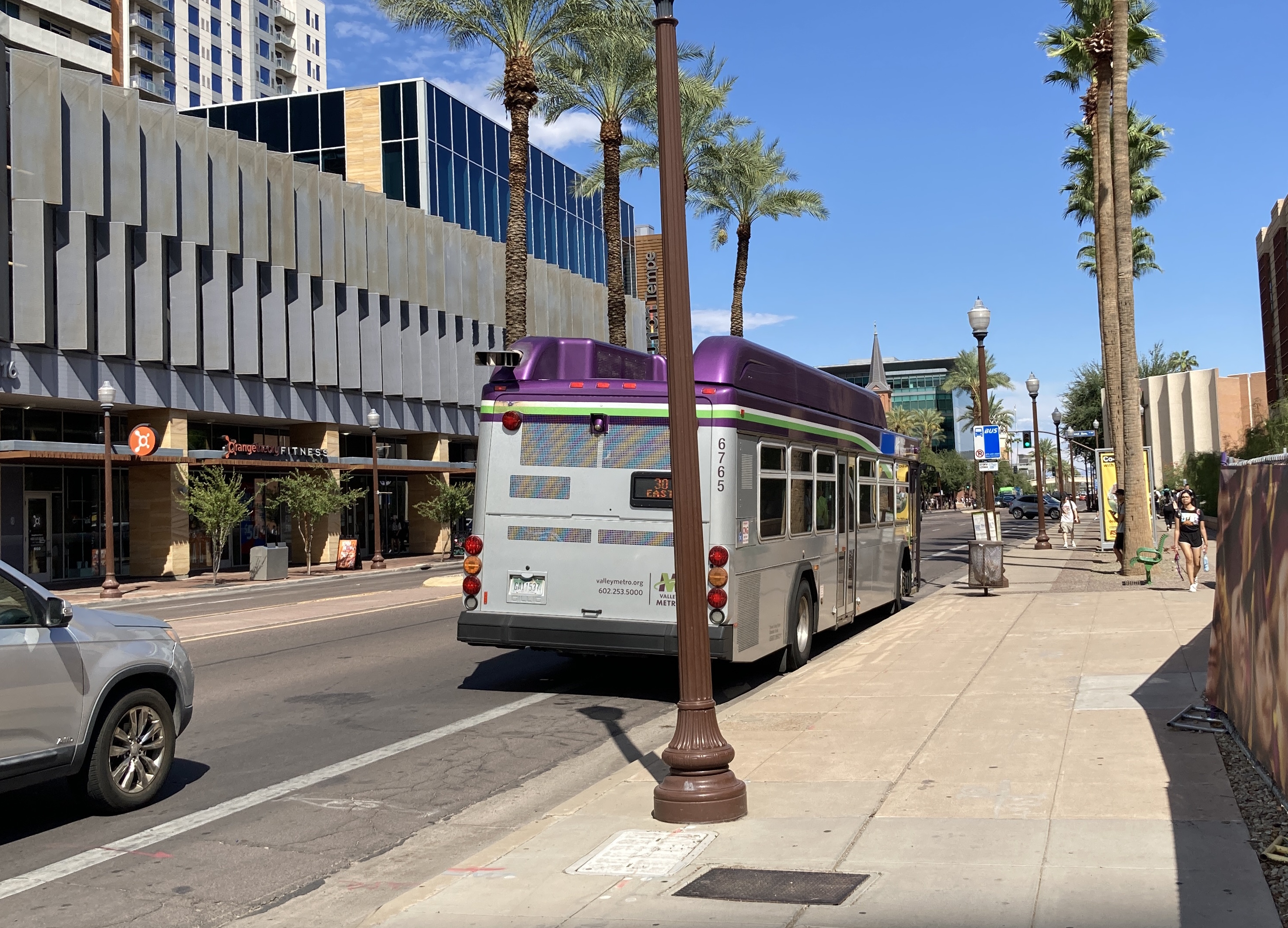 A gray and purple Valley Metro bus, with a white and green stripe, number 6765, traveling eastbound on University Drive in Tempe on route 30 to Power Road & University Drive