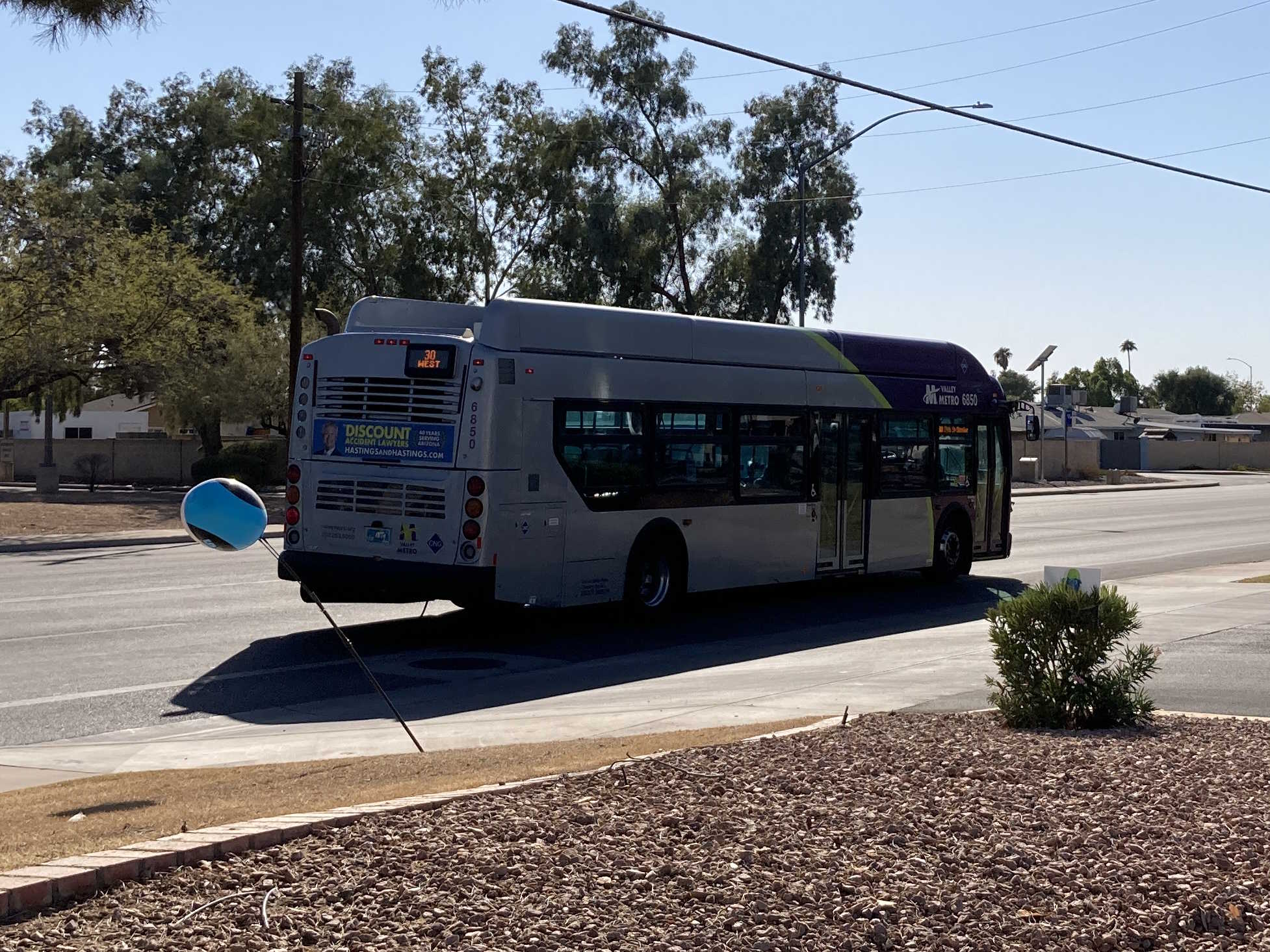 A gray and purple Valley Metro bus, with a green stripe, number 6850, traveling westbound on University Drive in Mesa on route 30 to 24th Street/Baseline Park and Ride