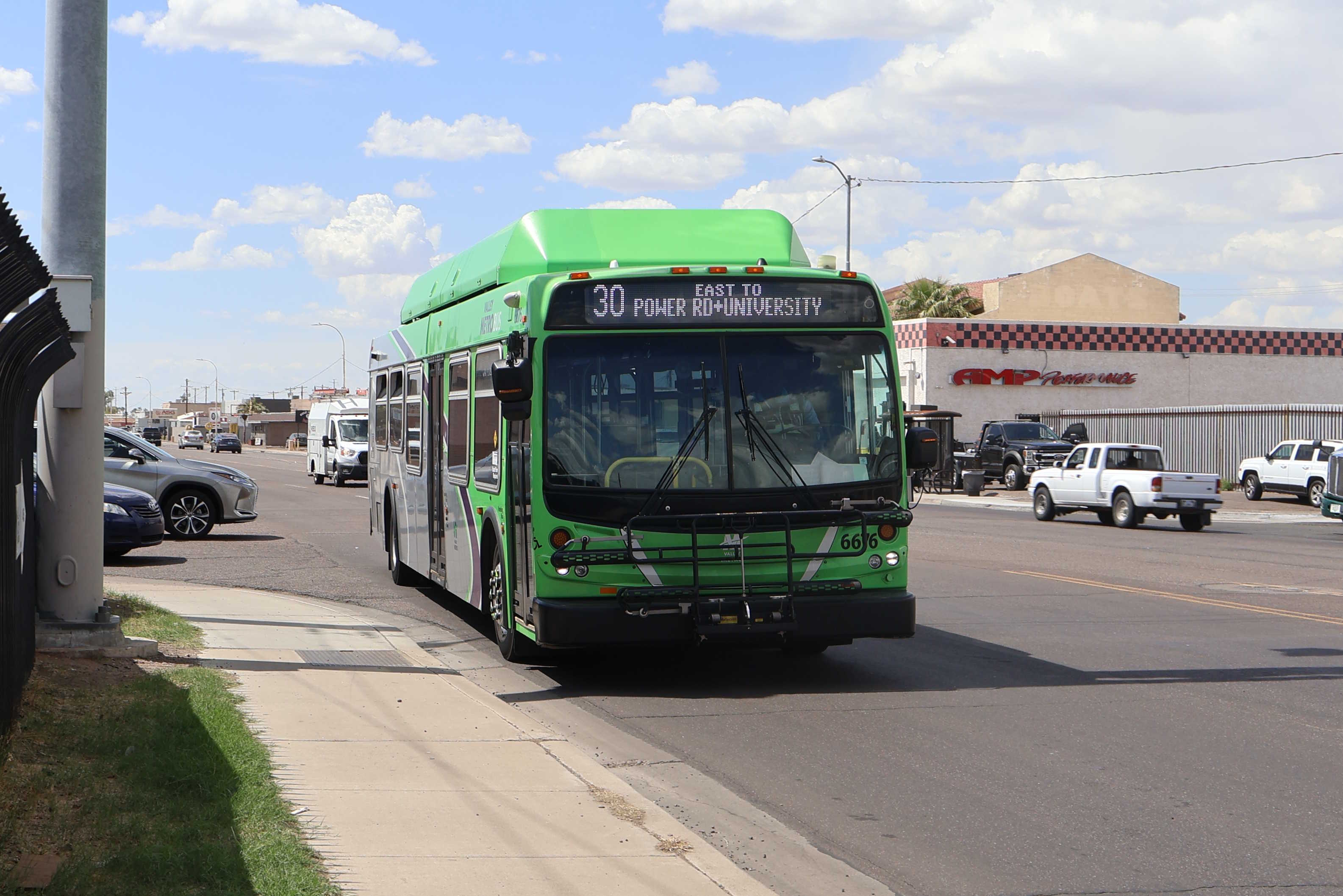 A green and gray Valley Metro bus, with a purple stripe, number 6676, traveling eastbound on University Drive in Phoenix on route 30 to Power Road and University Drive