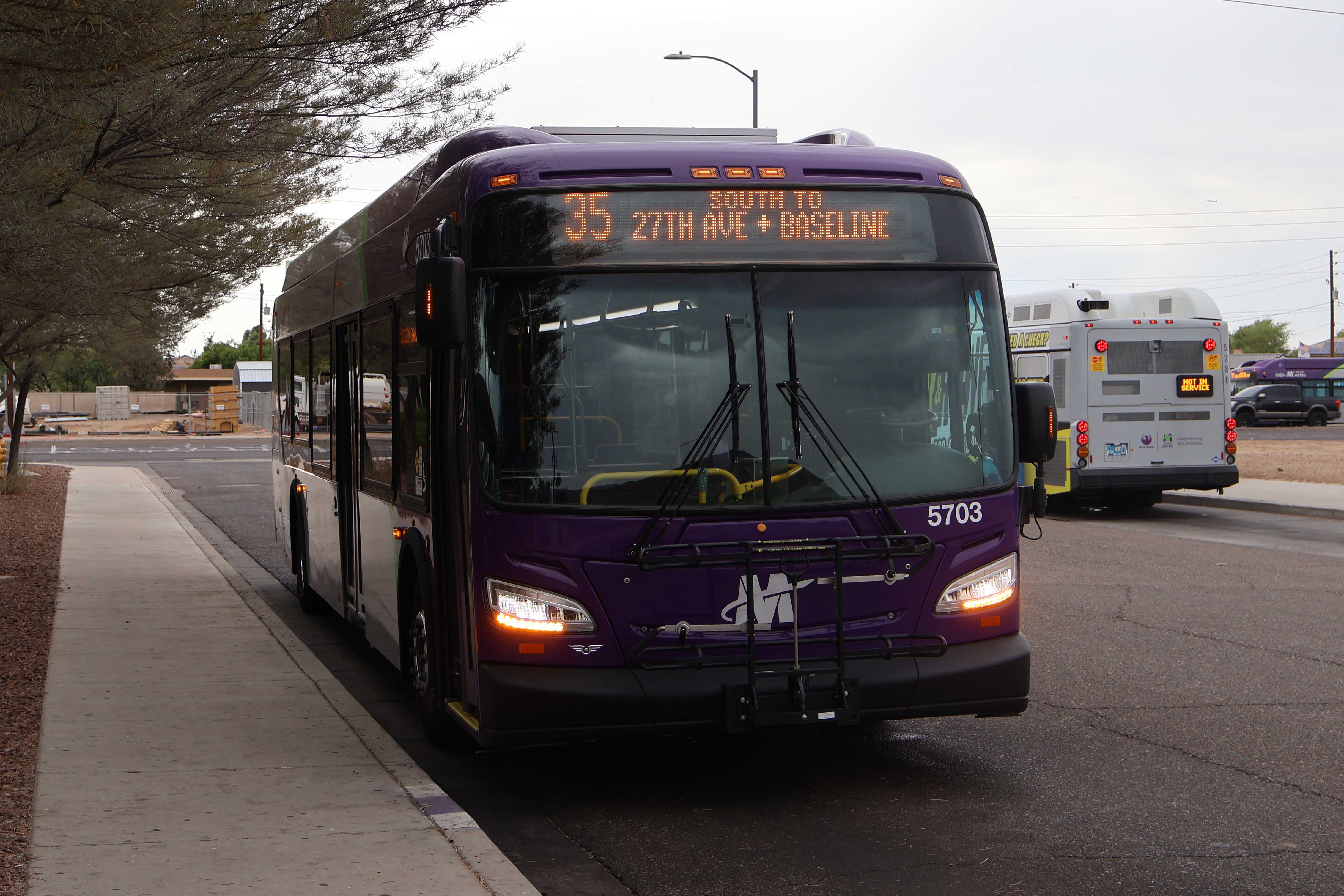 A gray and purple Valley Metro bus, with a green stripe, number 5703, traveling southbound on 27th Avenue in Phoenix on route 35 to 27th Avenue and Baseline Road