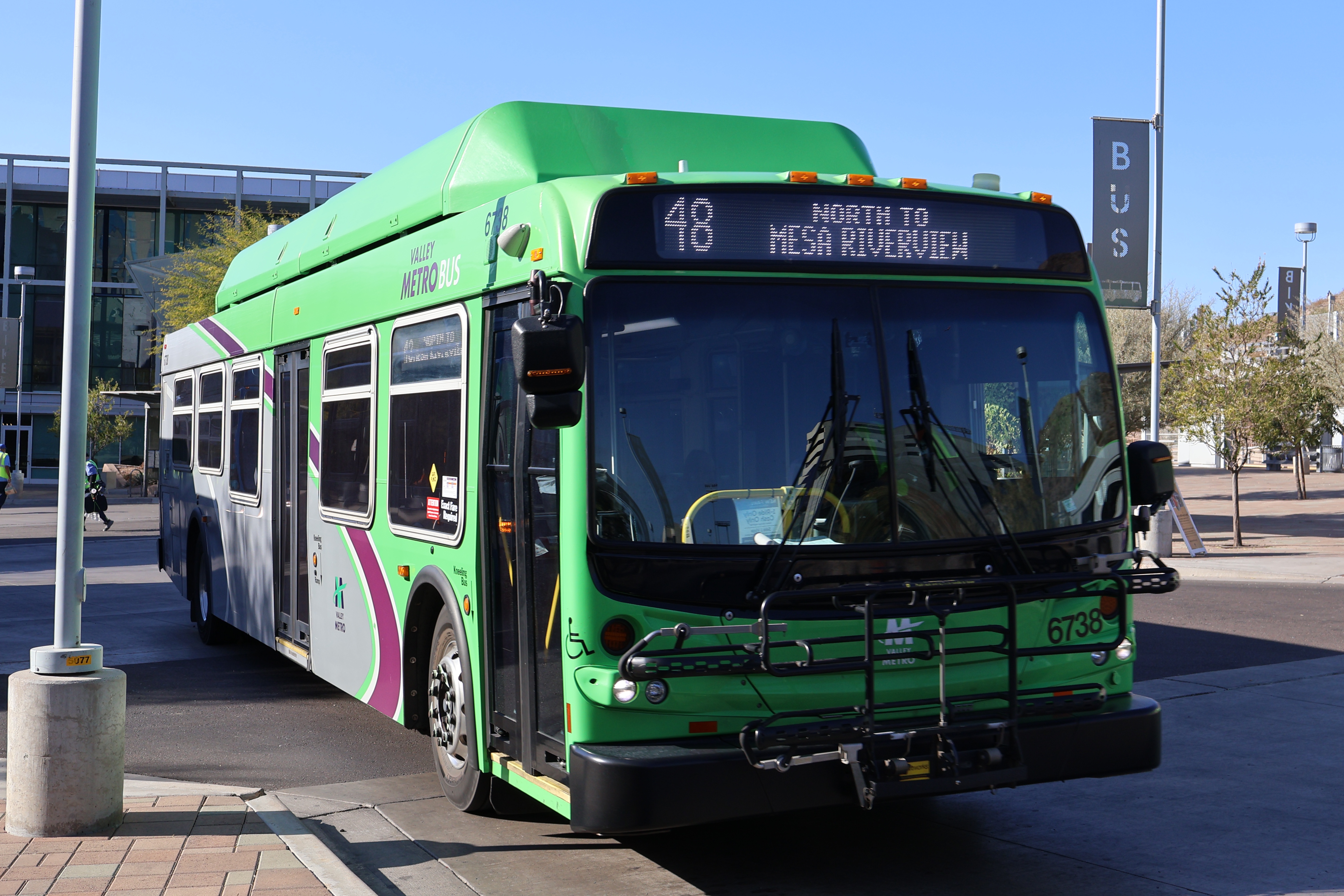 A gray and green Valley Metro bus, with a purple and white stripe, number 6738, at the Tempe Transportation Center, traveling route 48 to Mesa Riverview