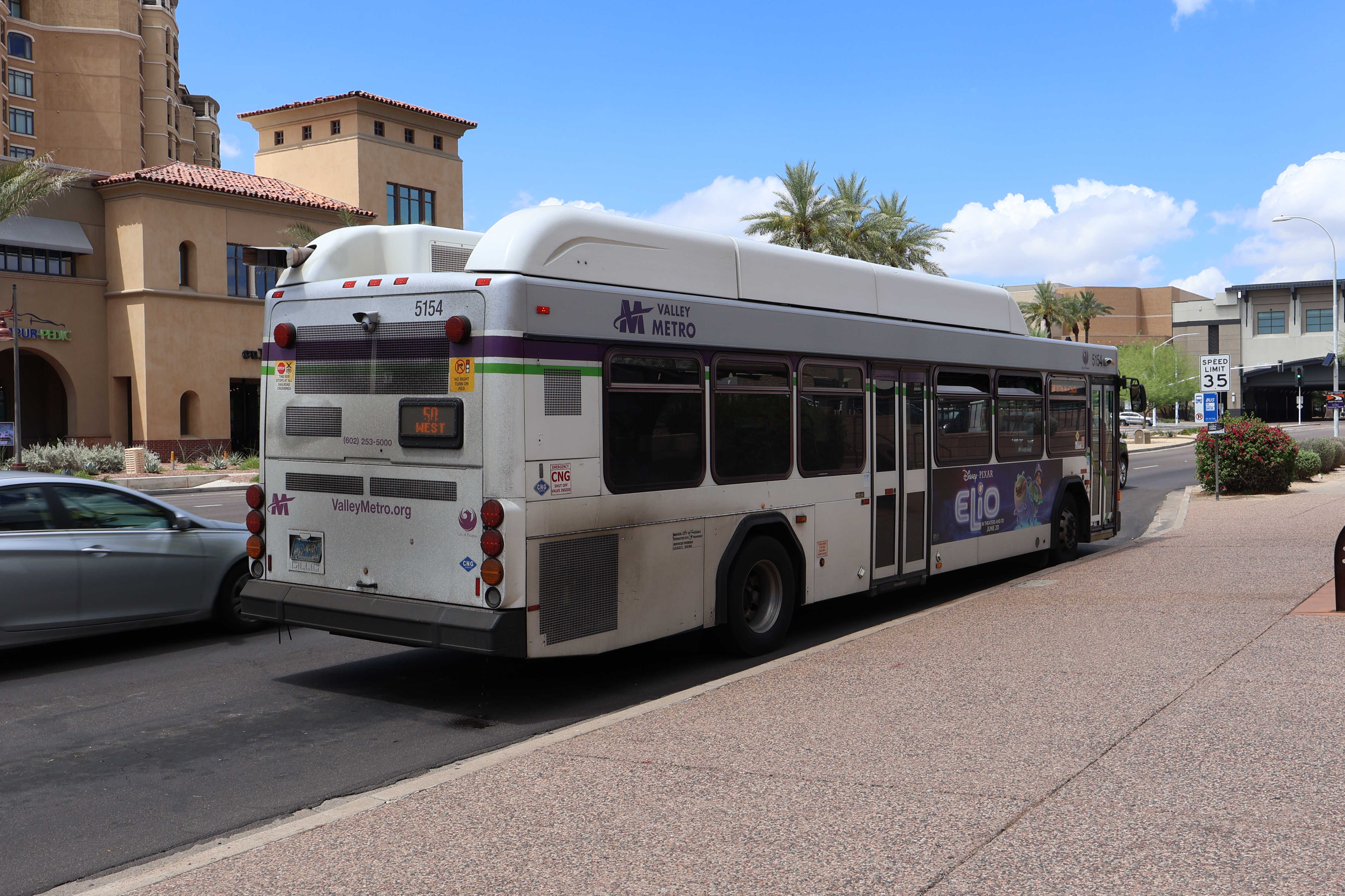 A white and gray Valley Metro bus, with purple and green accent colors, number 5154, traveling westbound on Camelback Road in Scottsdale on route 50 to Camelback Road and 107th Avenue