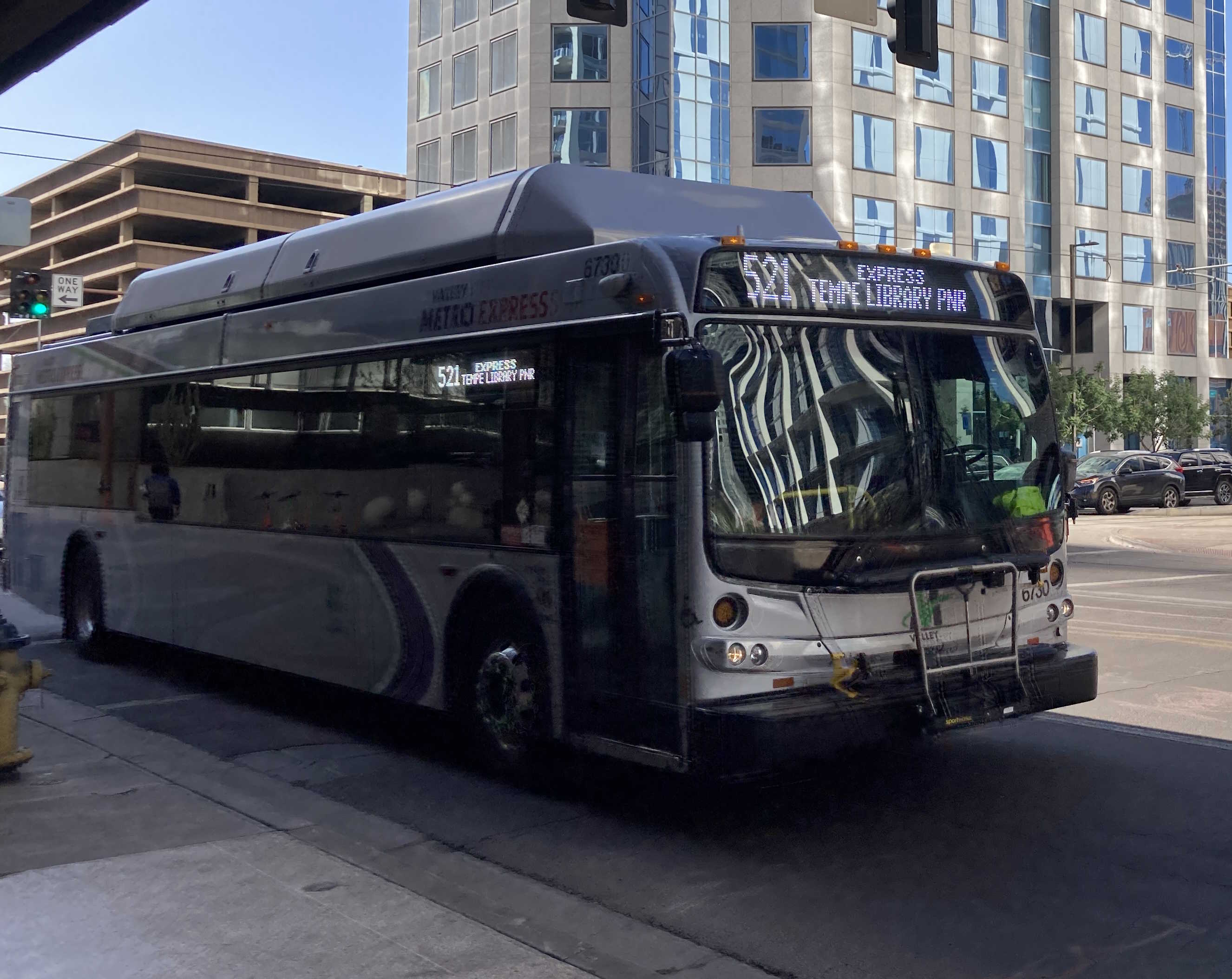 A silver Valley Metro bus, with green, purple, and white stripes, number 6730, traveling eastbound on Van Buren Street in Phoenix on route 521 to Tempe Library Park and Ride