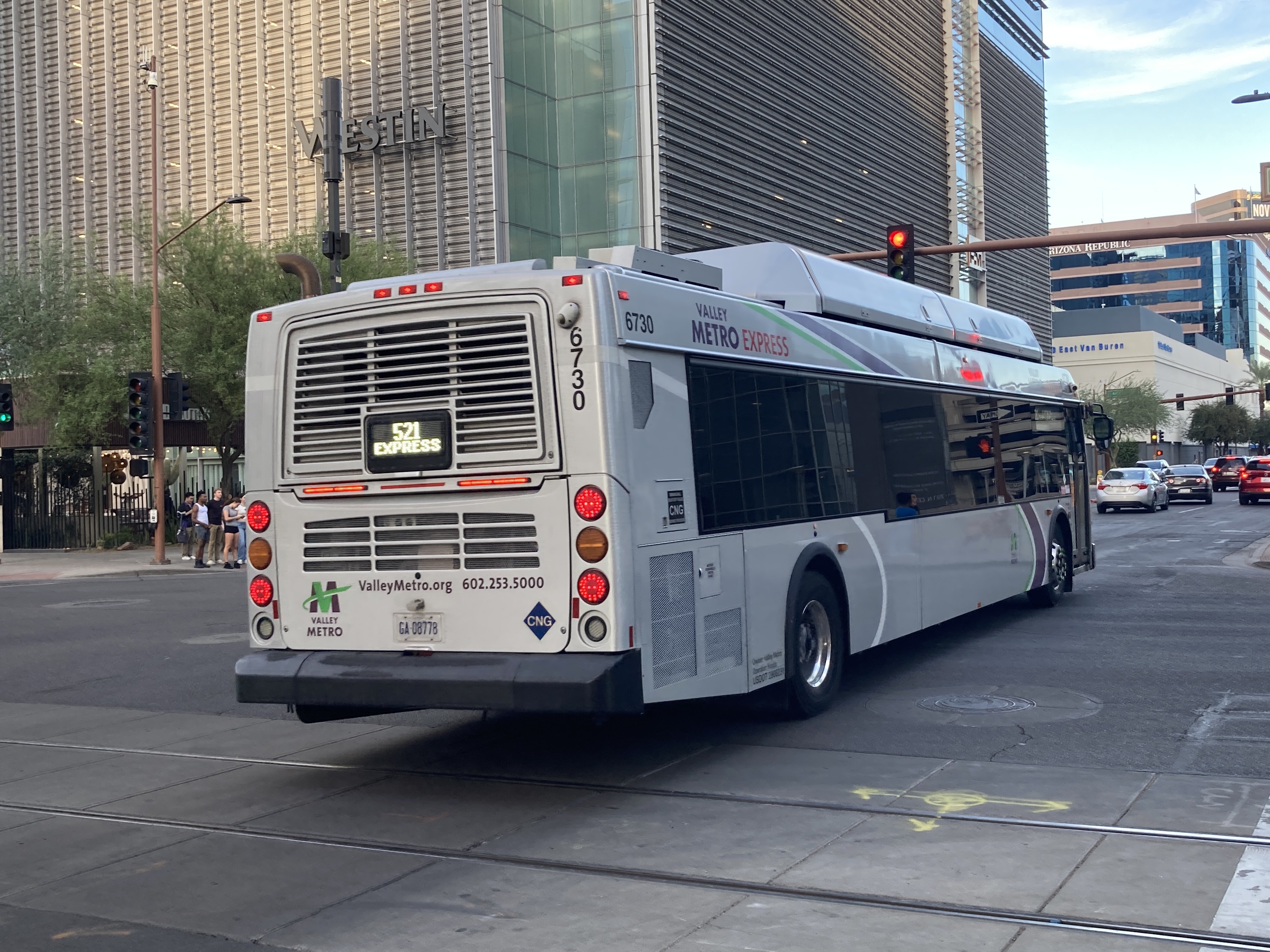 A silver Valley Metro bus, with green, purple, and white stripes, number 6730, traveling eastbound on Van Buren Street in Phoenix on route 521 to Tempe Library Park and Ride