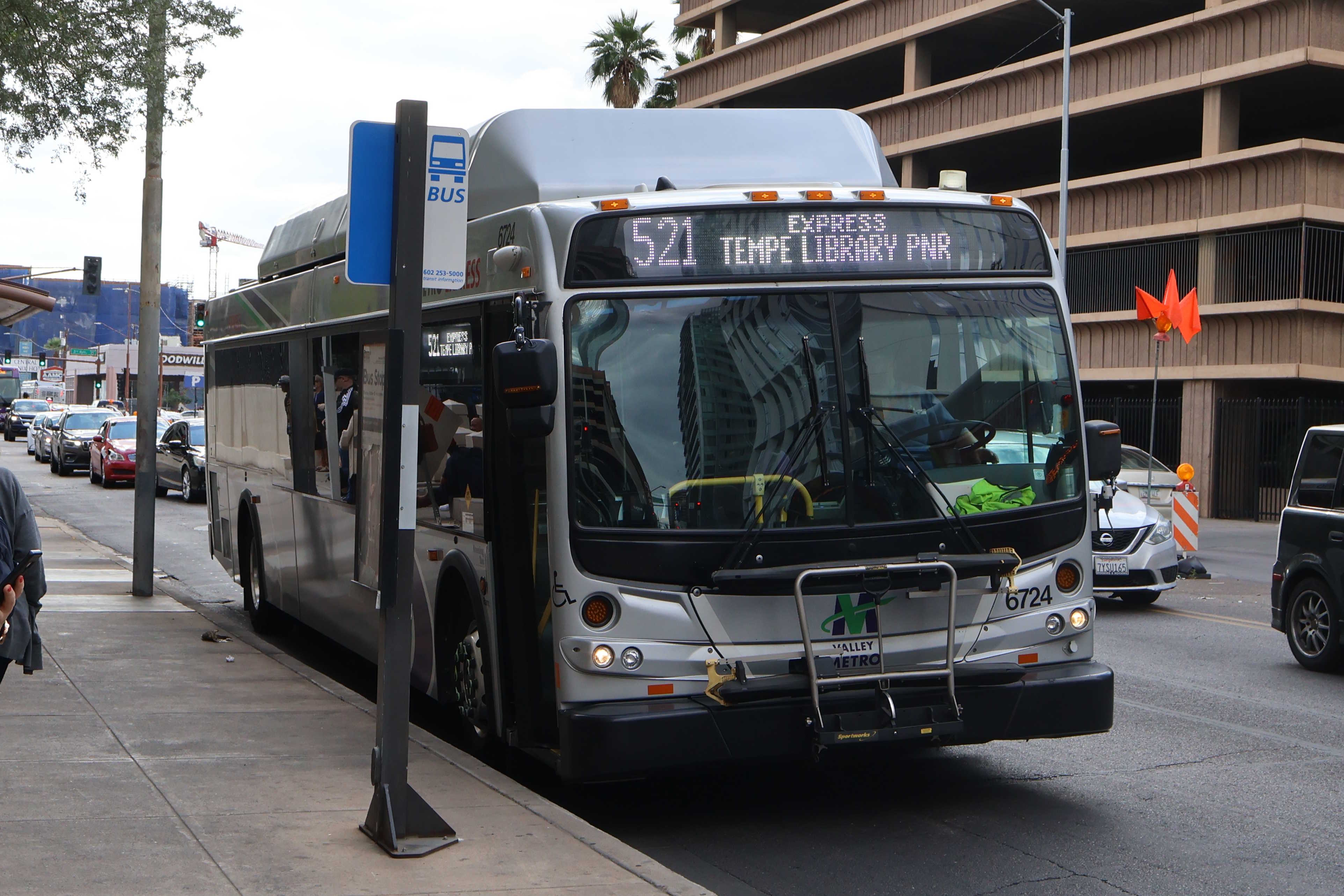 A silver Valley Metro bus, with green, purple, and white stripes, number 6724, traveling eastbound on Van Buren Street in Phoenix on route 521 to Tempe Library Park and Ride