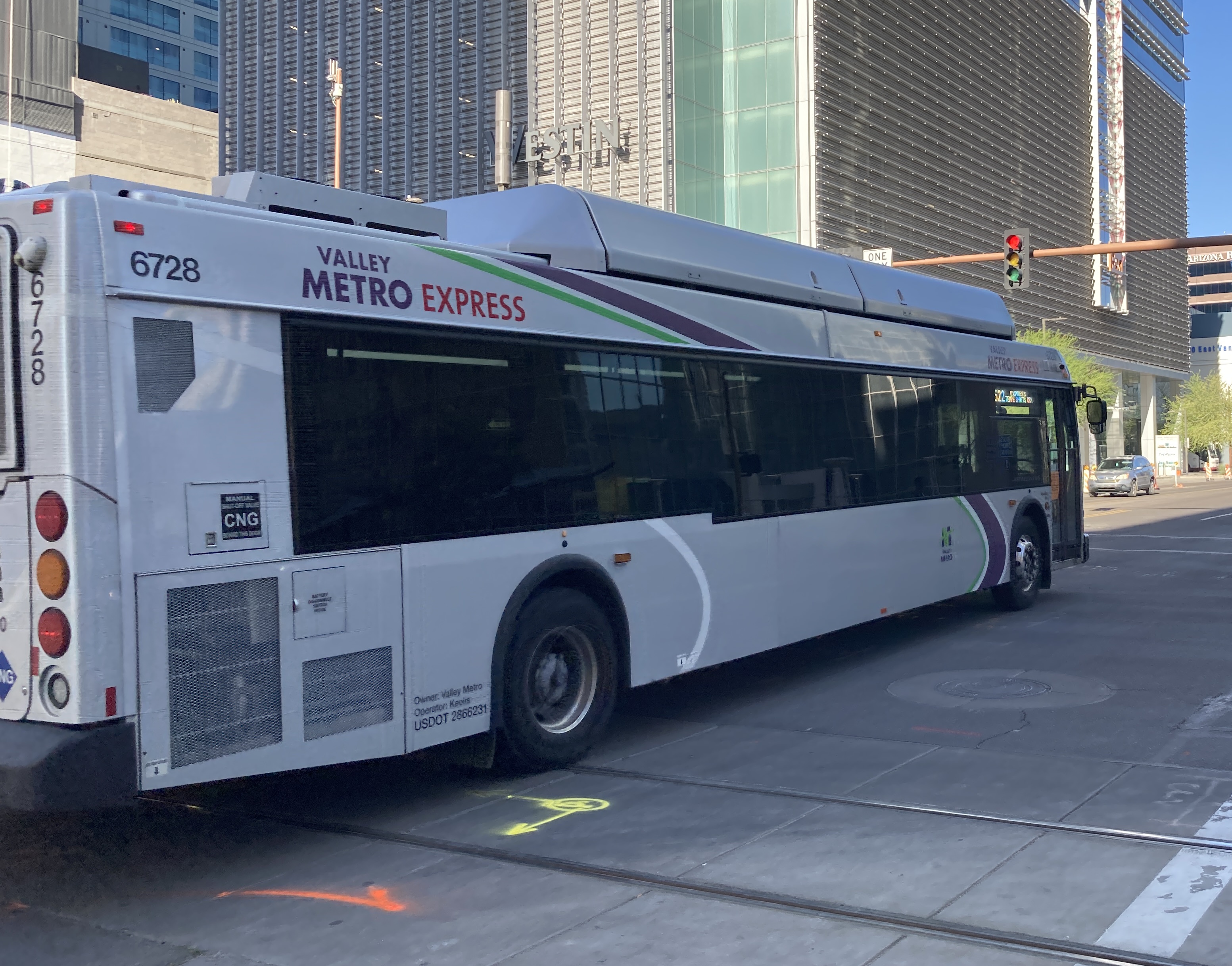 A silver Valley Metro bus, with green, purple, and white stripes, number 6728, traveling eastbound on Van Buren Street in Phoenix on route 522 to Tempe Sports Complex