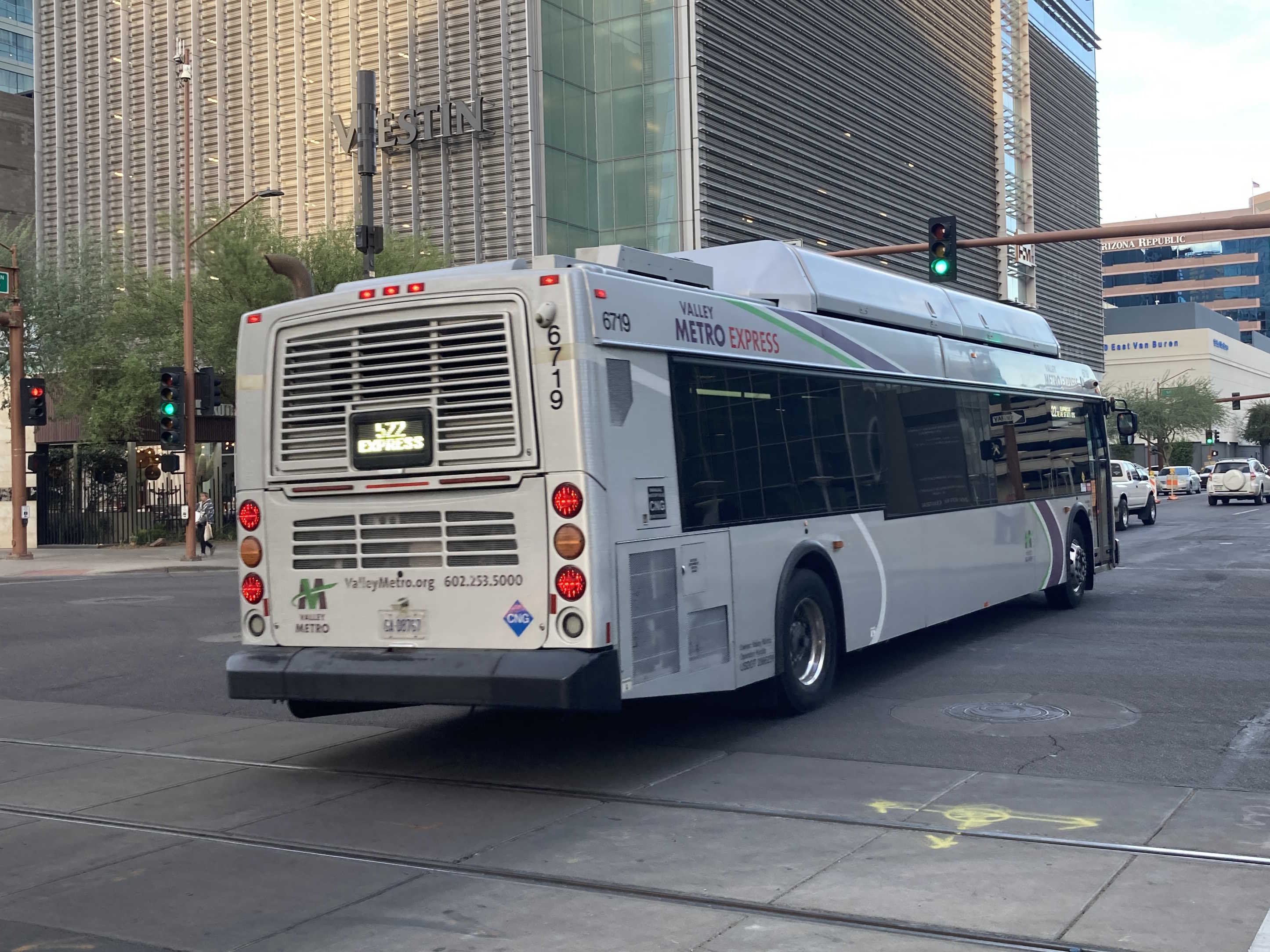 A silver Valley Metro bus, with green, purple, and white stripes, number 6719, traveling eastbound on Van Buren Street in Phoenix on route 522 to Tempe Sports Complex