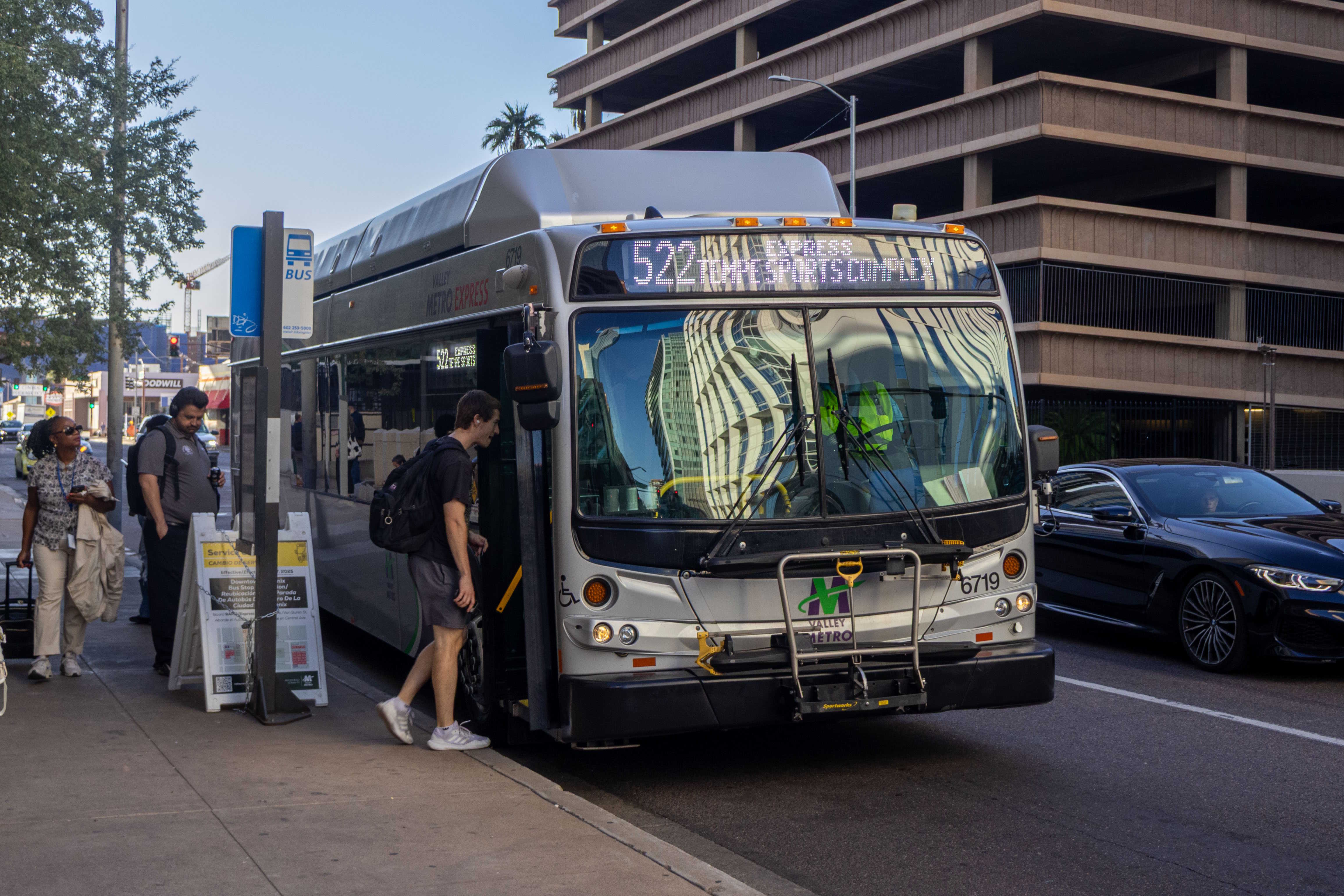 A silver Valley Metro bus, with green, purple, and white stripes, number 6719, traveling eastbound on Van Buren Street in Phoenix on route 522 to Tempe Sports Complex
