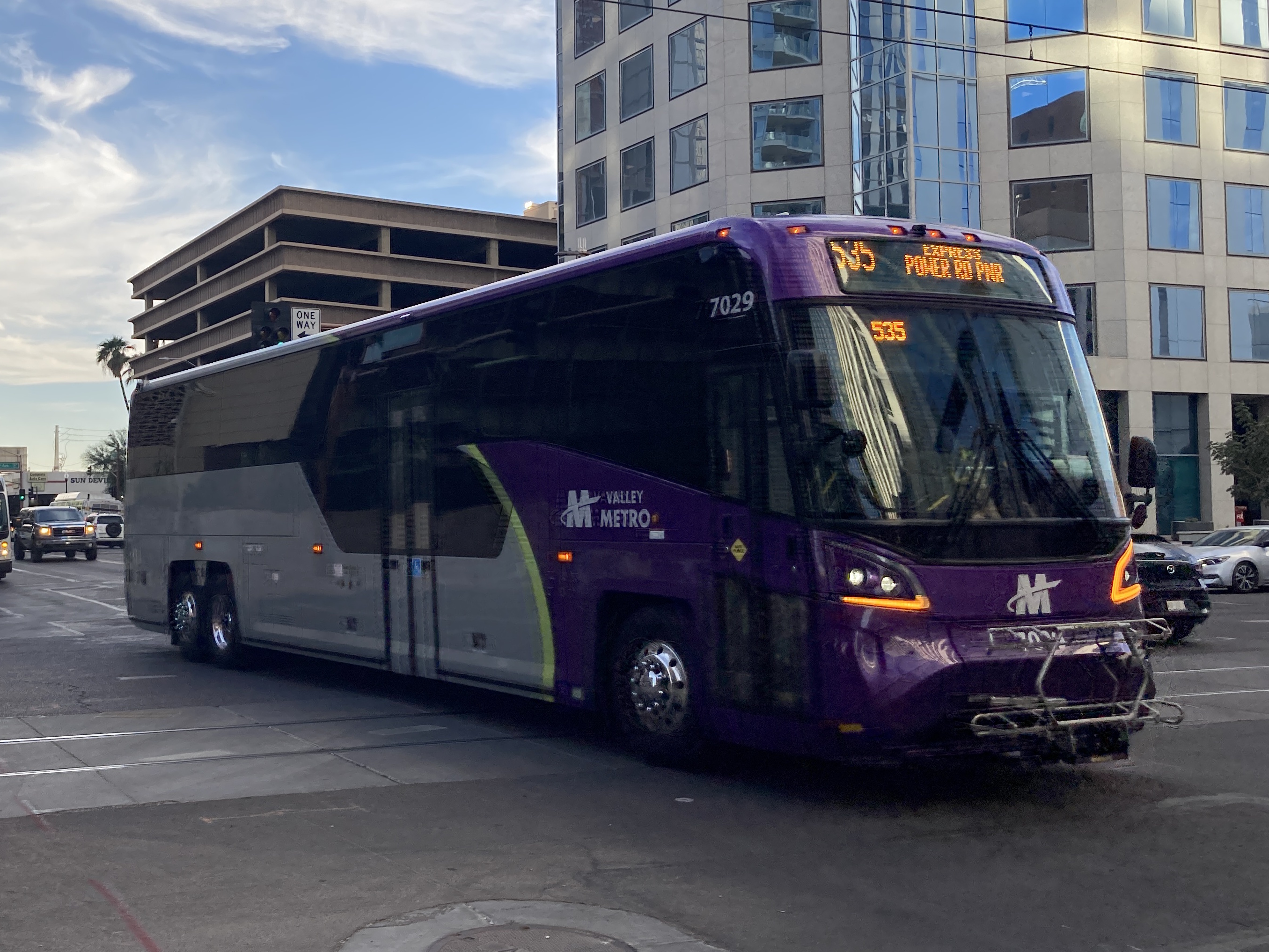 A gray and purple Valley Metro coach bus, with a green stripe, number 7029, traveling eastbound on Van Buren Street in Phoenix on route 535 to Power Road Park and Ride