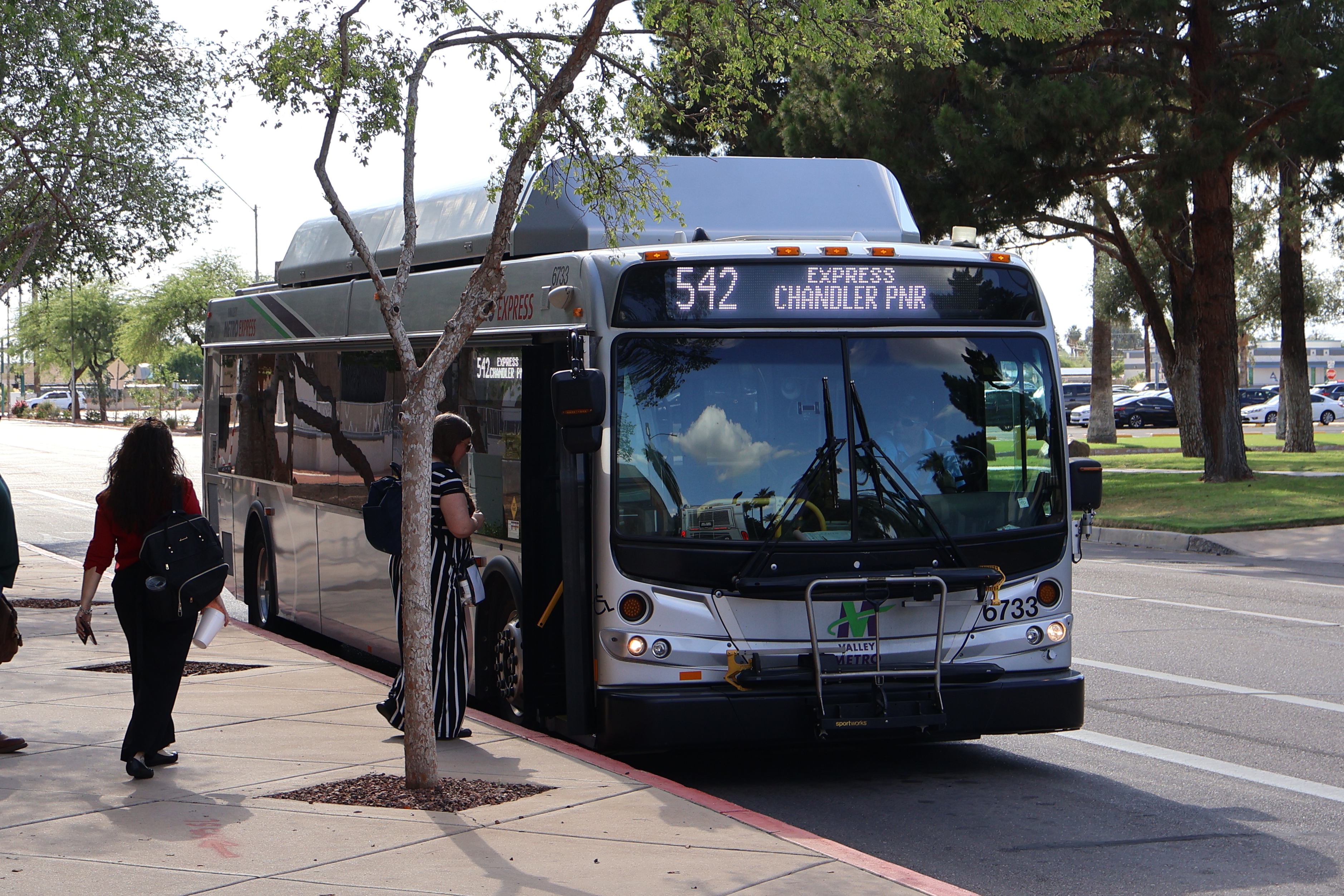 A silver Valley Metro bus, with green, purple, and white stripes, number 6733, traveling eastbound on Jefferson Street in Phoenix on route 542 to Chandler Park and Ride