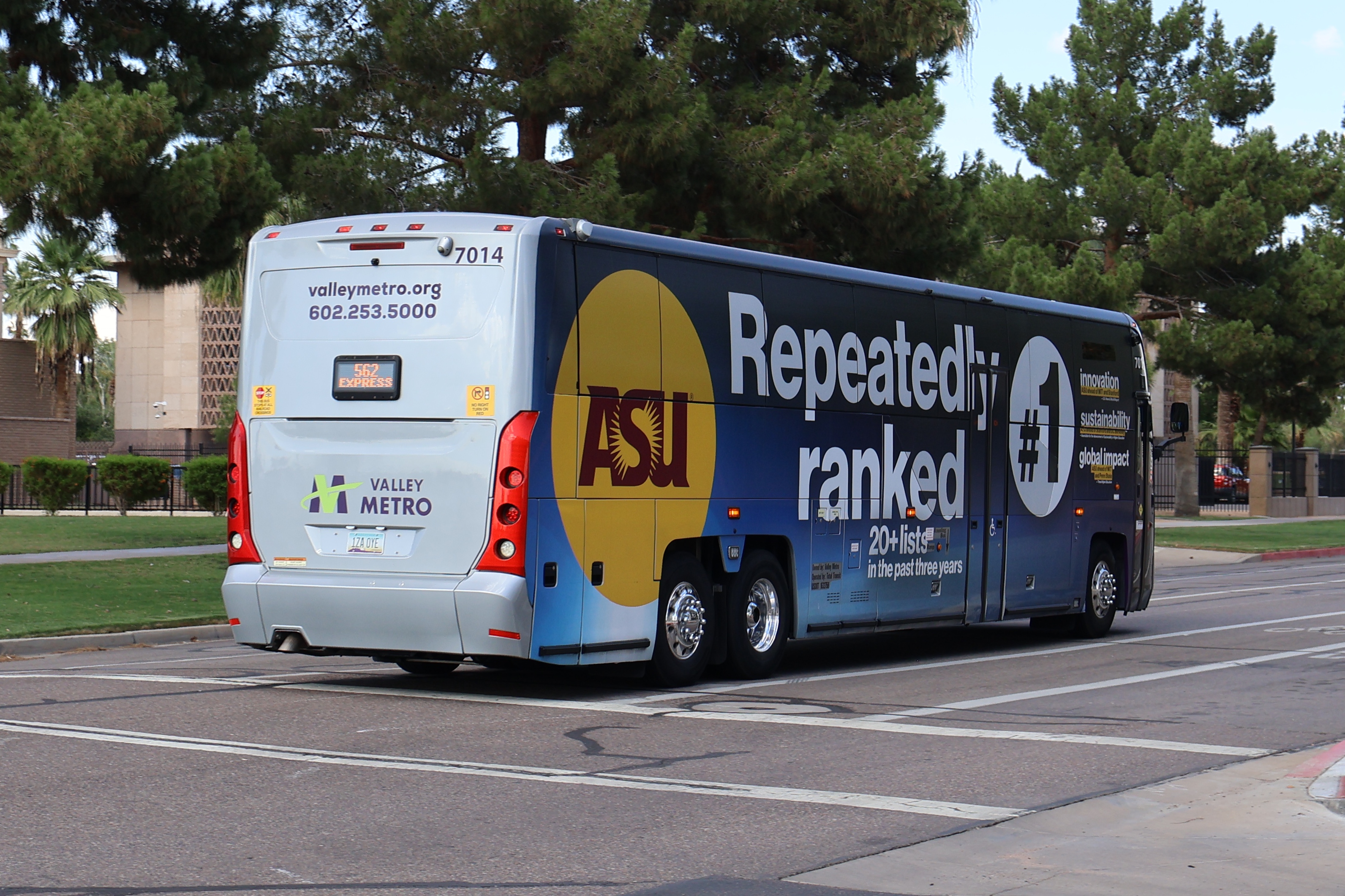 A gray and purple Valley Metro coach bus, with a green stripe, number 7014, traveling eastbound on Jefferson Street in Phoenix on route 562 to Goodyear Park and Ride