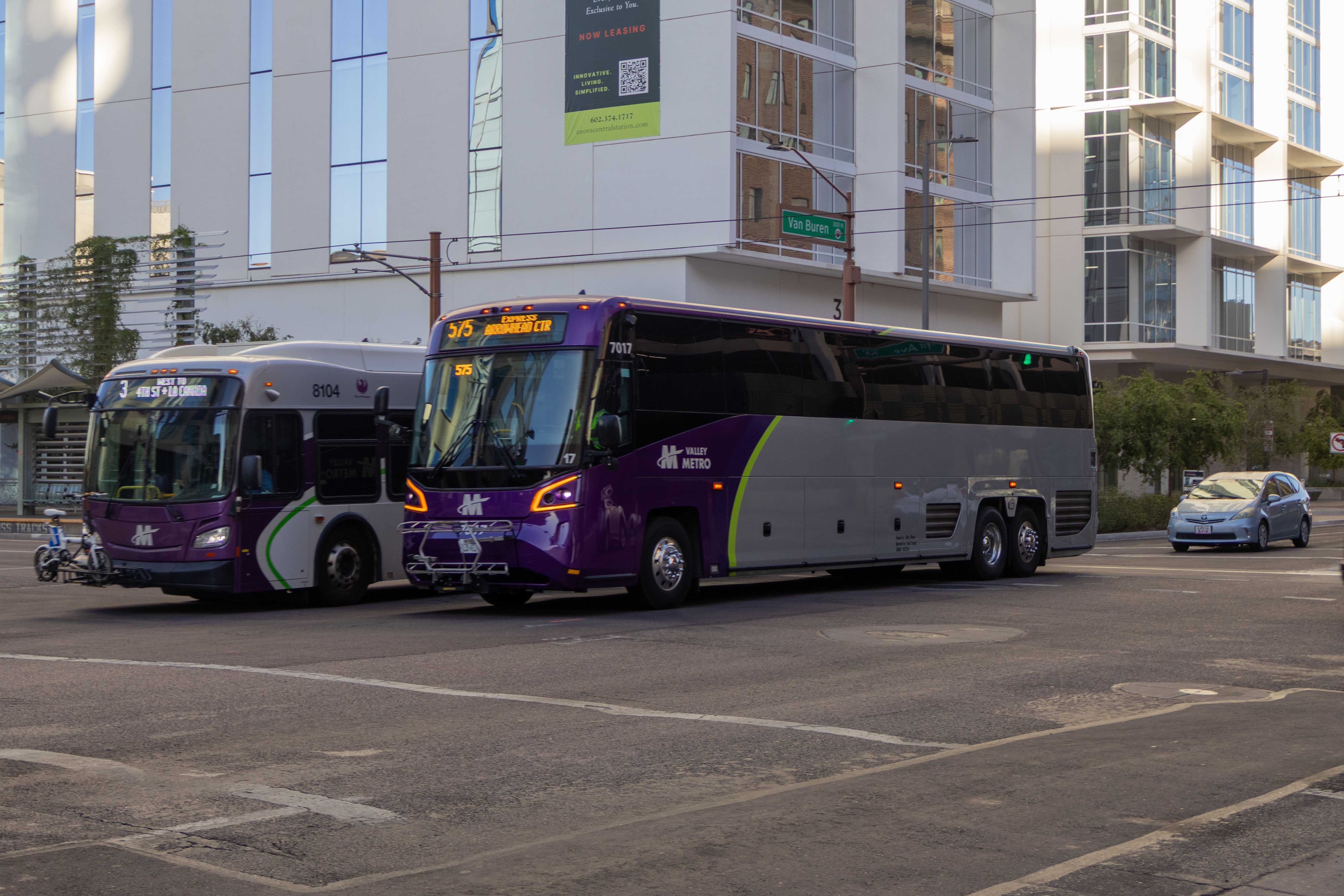 A gray and purple Valley Metro coach bus, with a green stripe, number 7017, traveling westbound on Van Buren Street in Phoenix on route 575 to Arrowhead Mall Transit Center