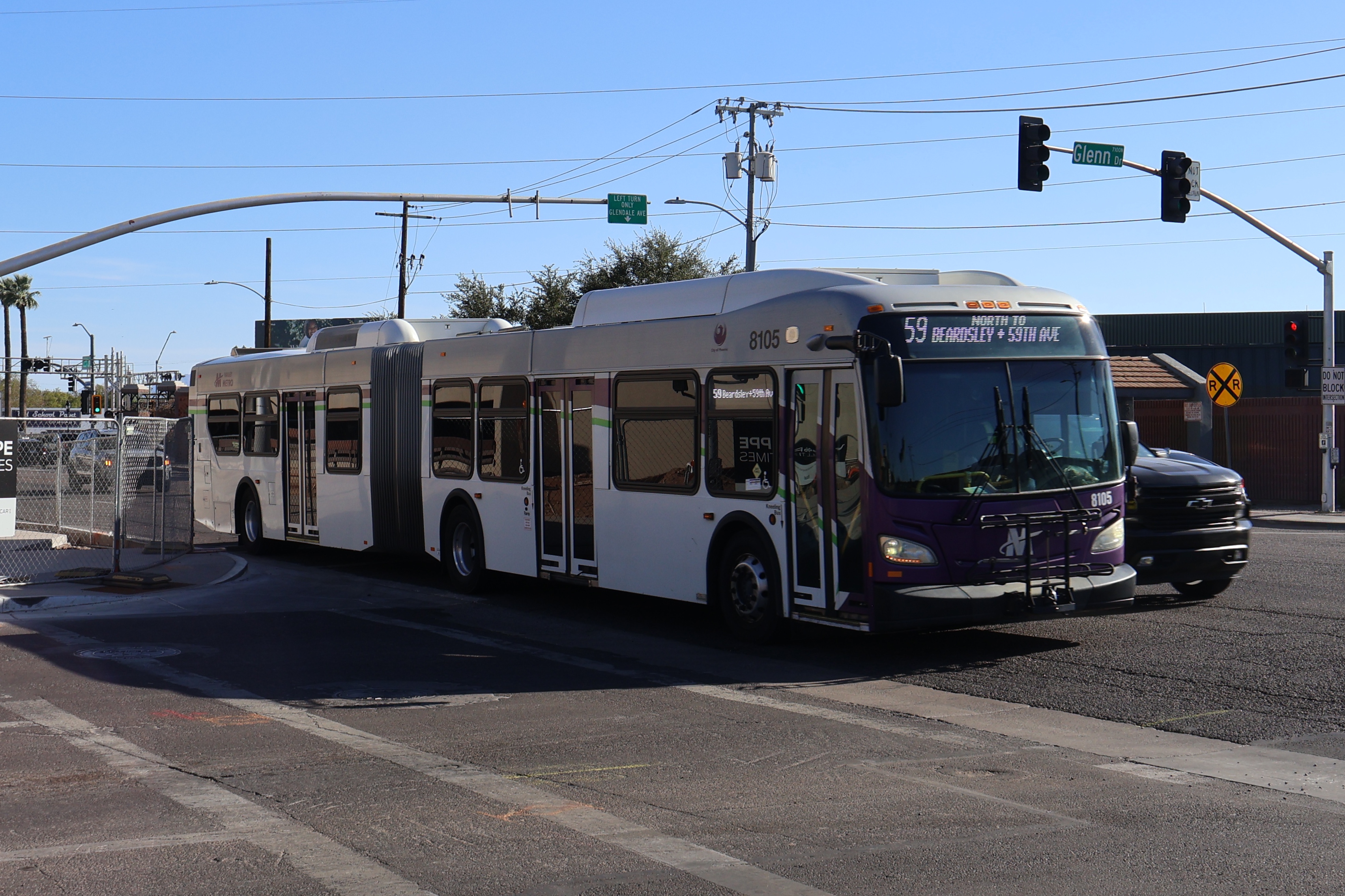 A white and gray articulated Valley Metro bus, with purple and green accent colors, number 8105, traveling northbound on 59th Avenue in Glendale on route 59 to 59th Avenue and Beardsley Road
