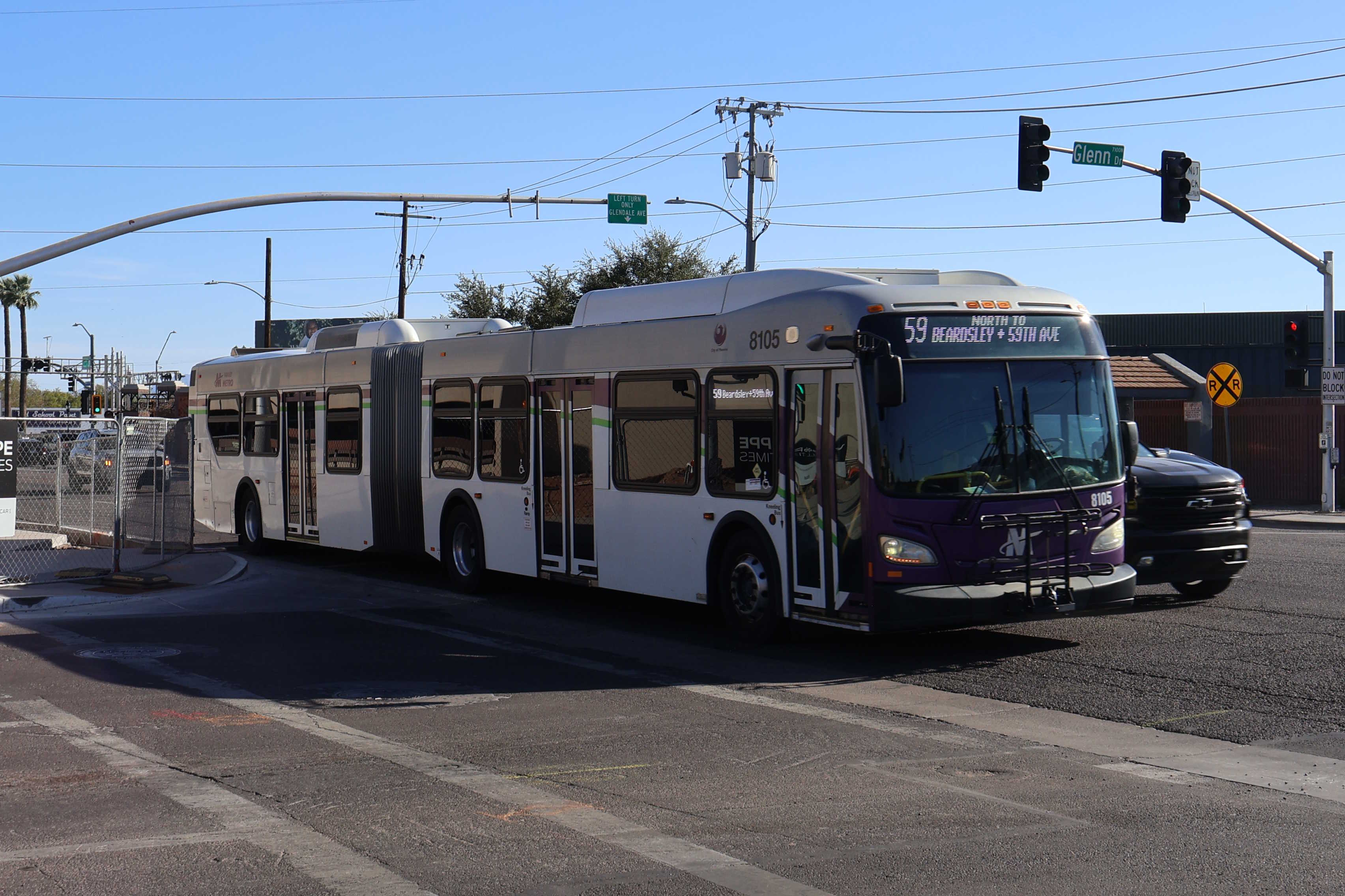 A white and gray articulated Valley Metro bus, with purple and green accent colors, number 8105, traveling northbound on 59th Avenue in Glendale on route 59 to 59th Avenue and Beardsley Road