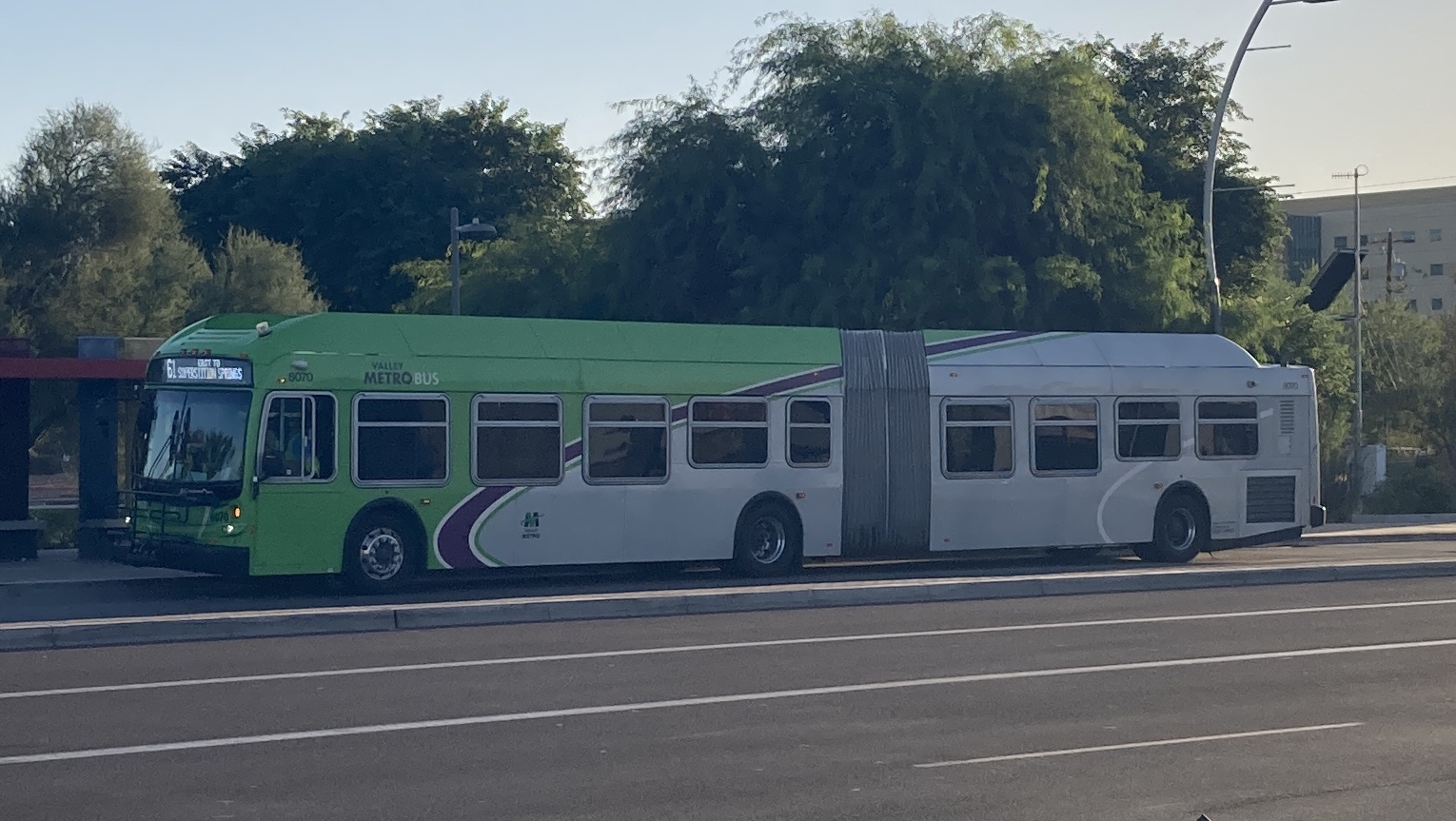 A gray and green articulated Valley Metro bus with a purple and white stripe, number 8070, traveling eastbound on Southern Avenue in Mesa on route 61 to Superstition Springs Transit Center