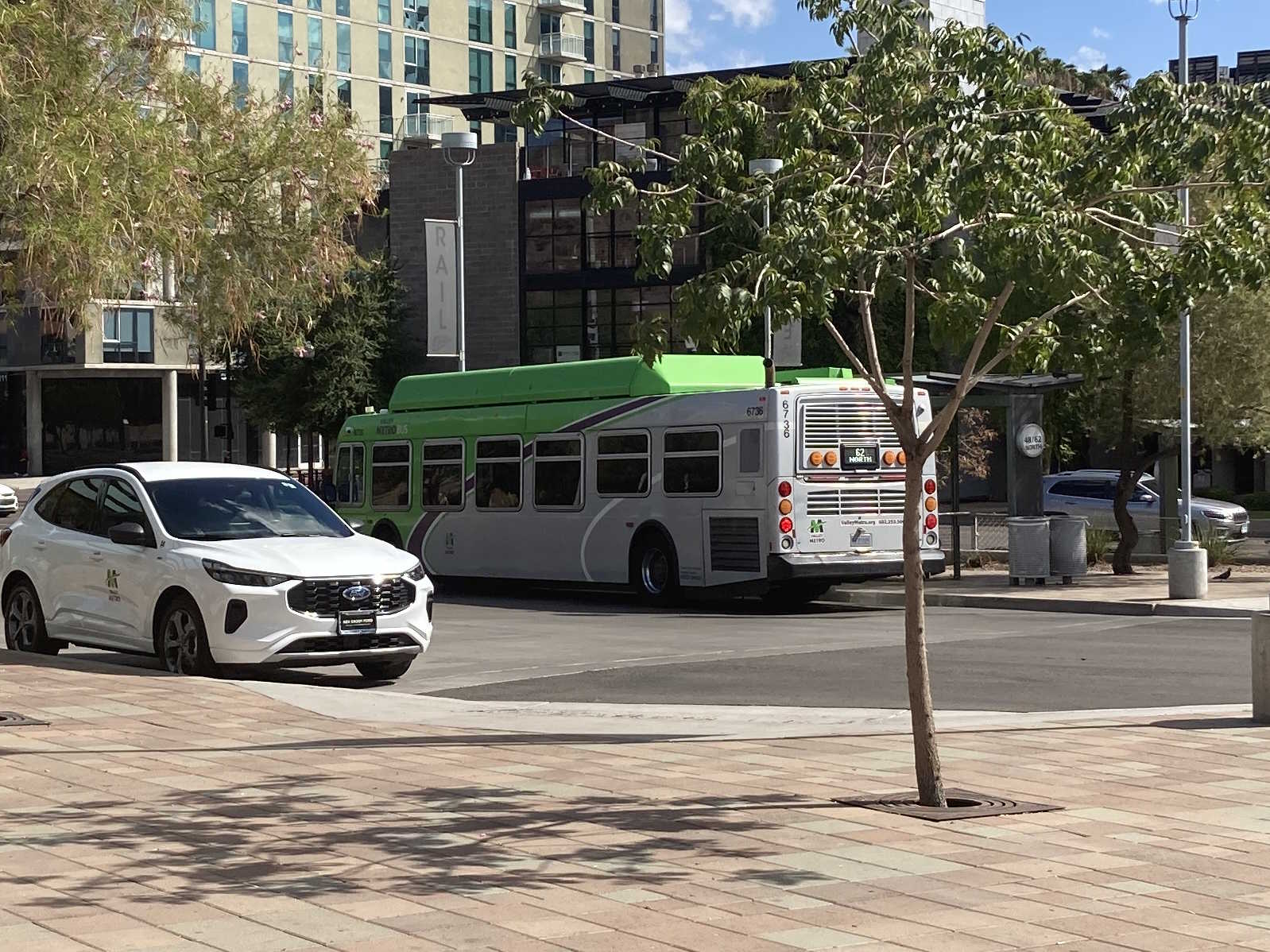 A gray and green Valley Metro bus, with a purple and white stripe, number 6736, at the Tempe Transportation Center, traveling route 62 to Tempe Marketplace