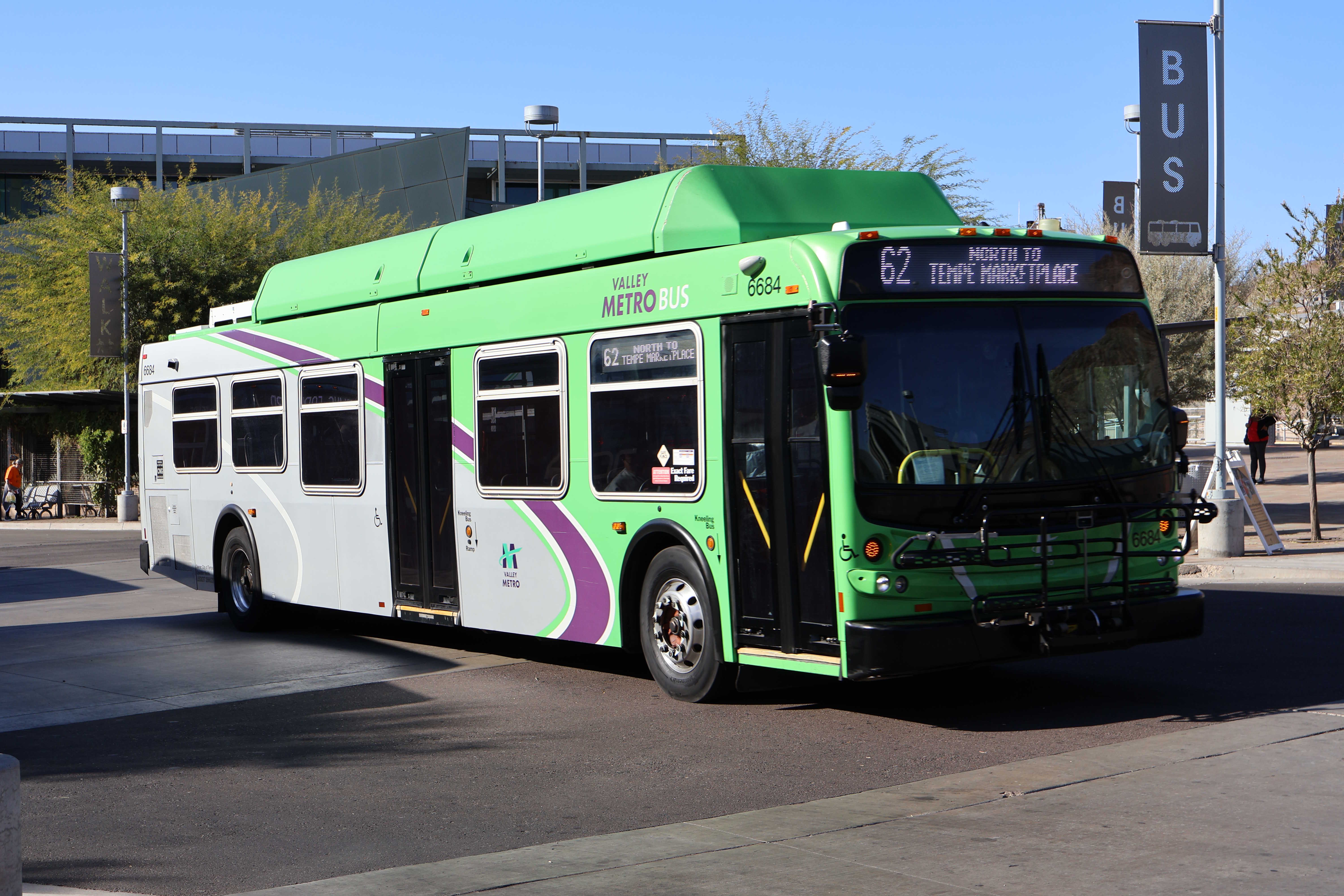 A gray and green Valley Metro bus, with a purple and white stripe, number 6684, at the Tempe Transportation Center, traveling route 62 to Tempe Marketplace