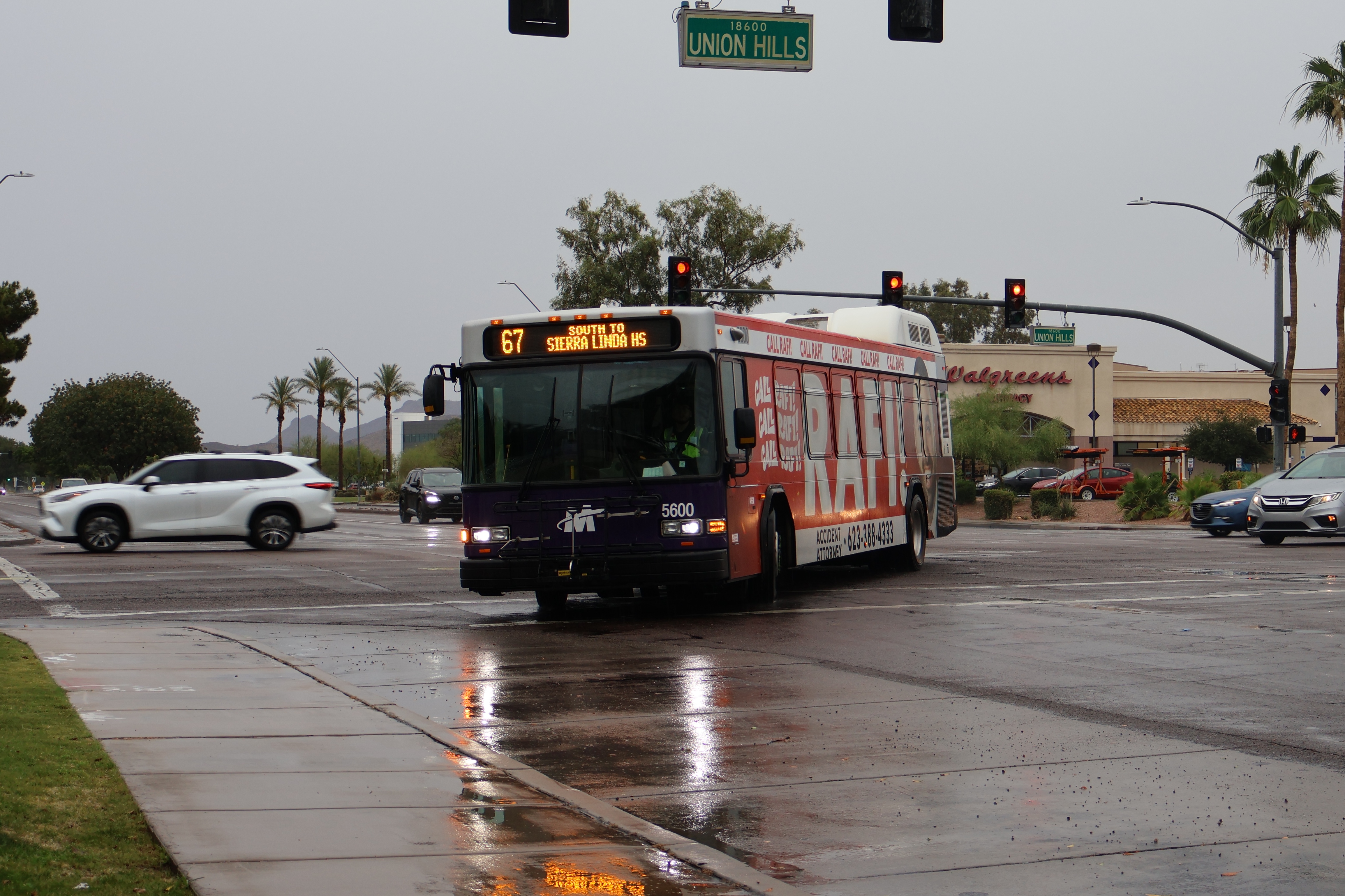 A white and gray Valley Metro bus, with purple and green accent colors, number 5600, traveling southbound on 67th Avenue in Glendale on route 67 to Sierra Linda High School