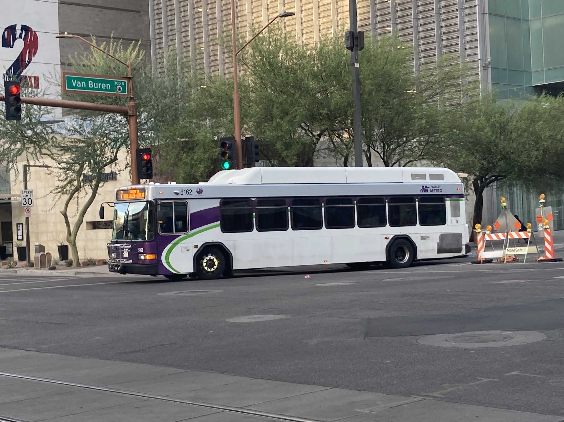 A white and gray Valley Metro bus, with purple and green accent colors, number 5162, traveling westbound on Van Buren Street in Phoenix on route 7 to Deer Valley Road and 19th Avenue