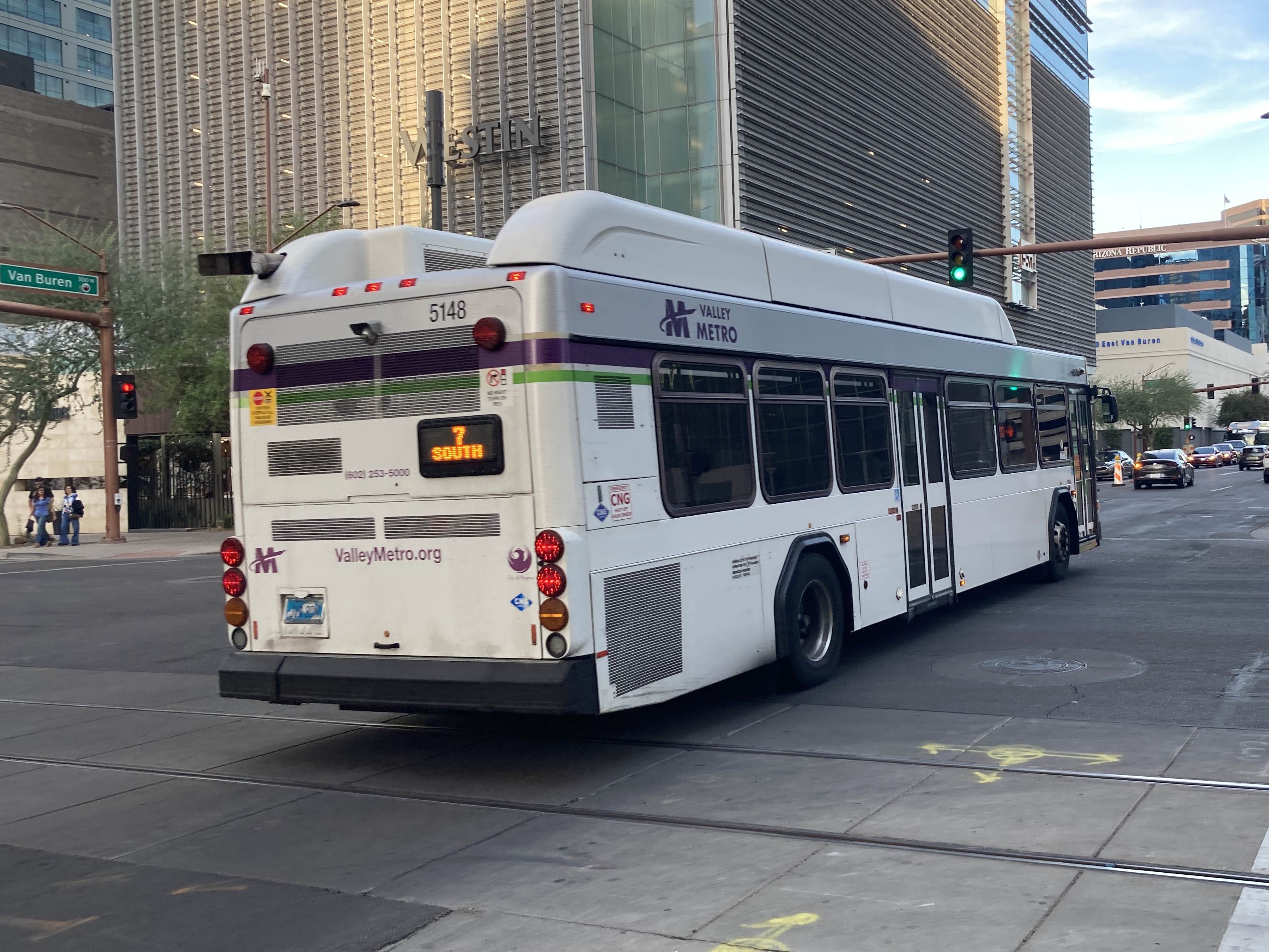 A white and gray Valley Metro bus, with purple and green accent colors, number 5148, traveling eastbound on Van Buren Street in Phoenix on route 7 to 7th Street and Dobbins Road