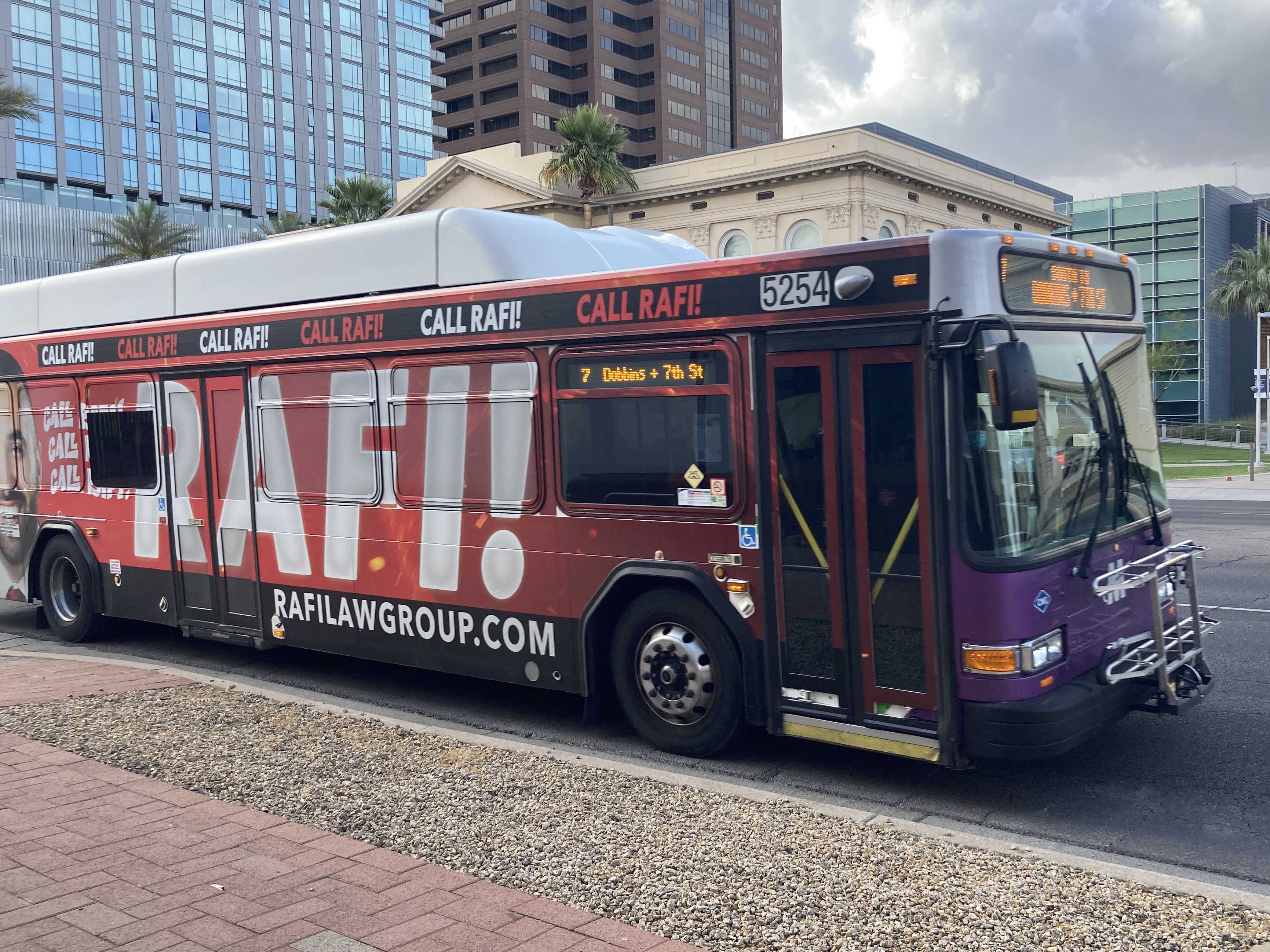 A white and gray Valley Metro bus, with purple and green accent colors, number 5254, traveling eastbound on Van Buren Street in Phoenix on route 7 to 7th Street and Dobbins Road