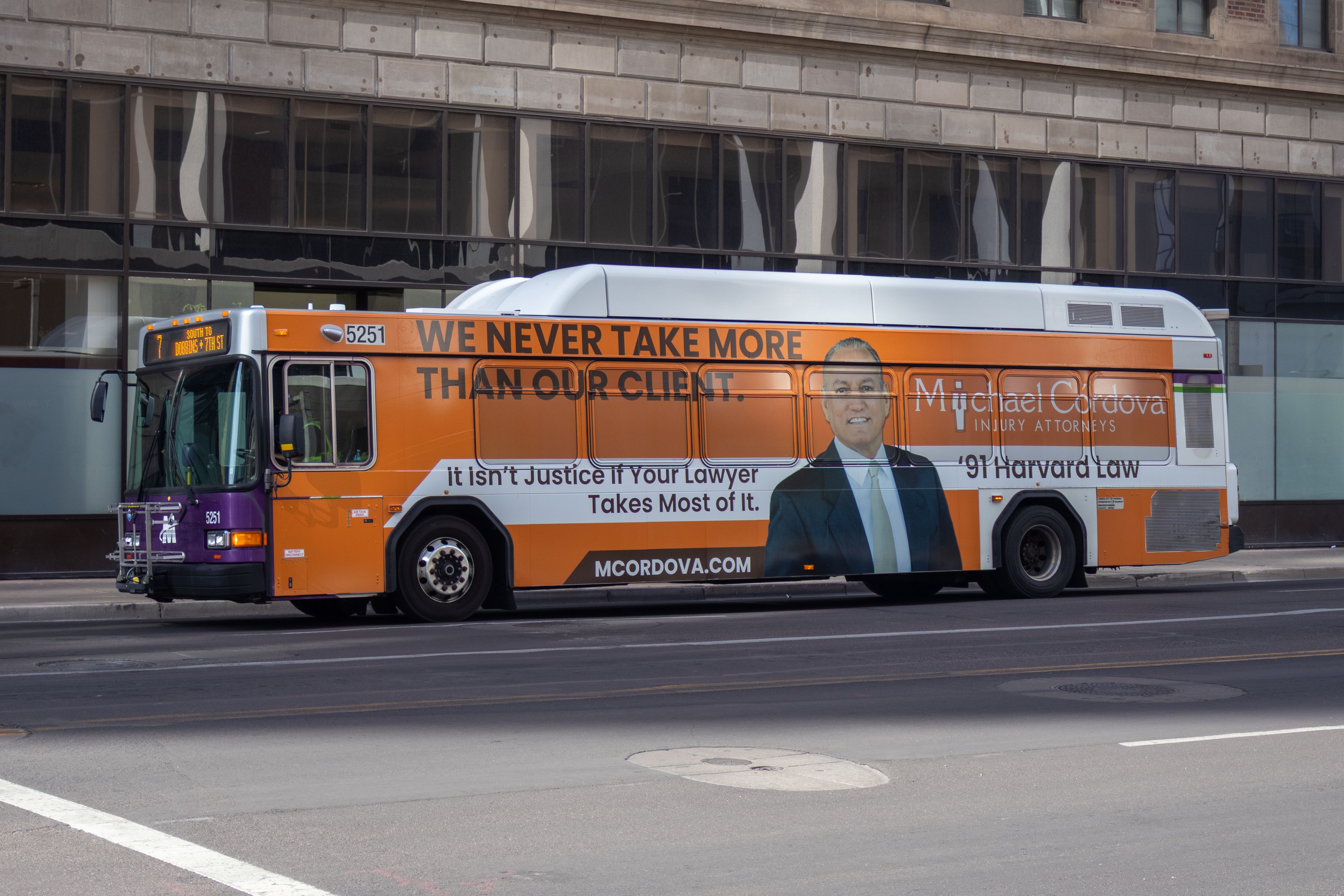 A white and gray articulated Valley Metro bus, with purple and green accent colors, number 5251, traveling eastbound on Van Buren Street in Phoenix on route 7 to 7th Street and Dobbins Road