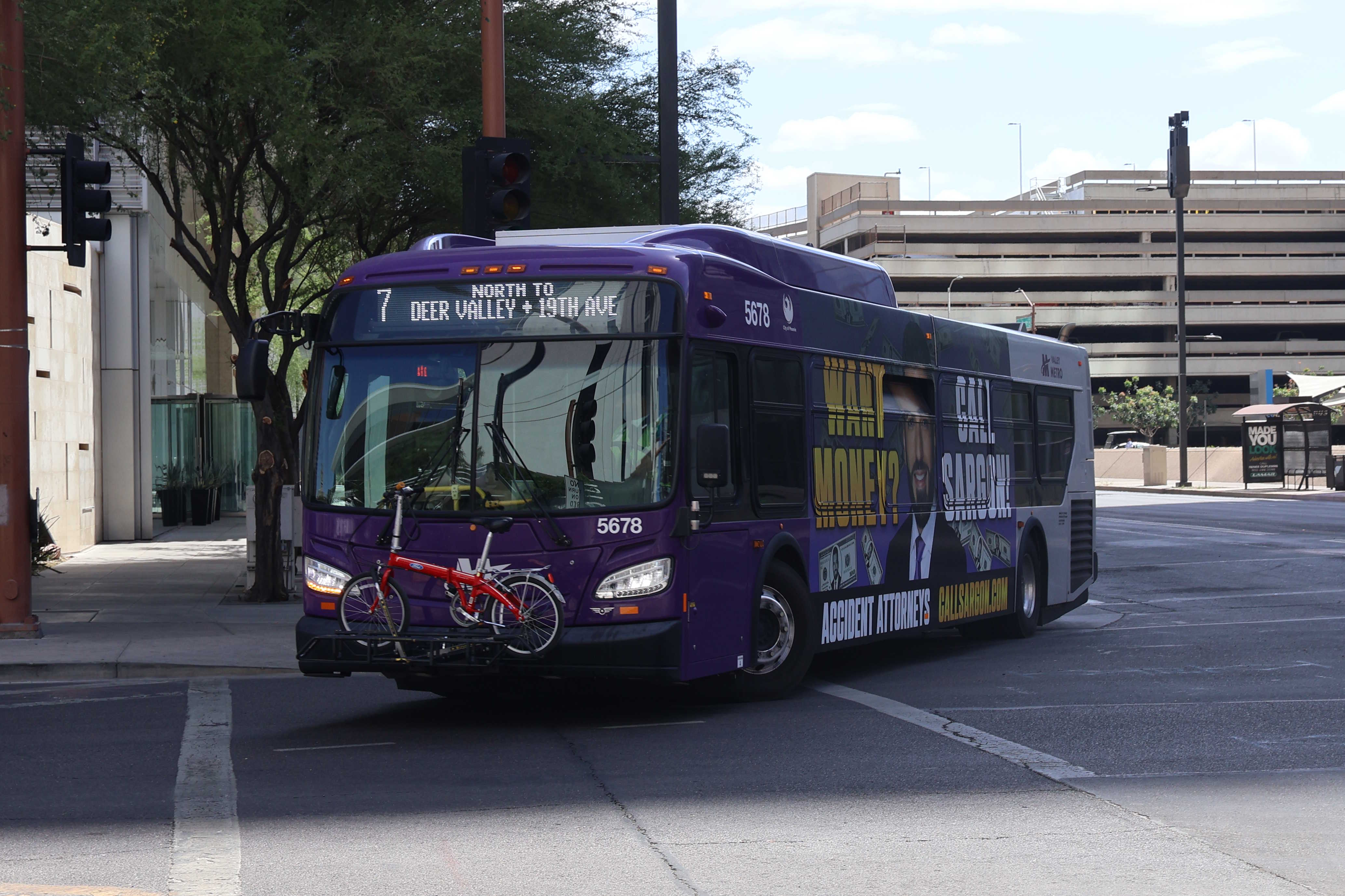 A gray and purple Valley Metro bus, with a green stripe, number 5678, traveling westbound on Van Buren Street in Phoenix on route 7 to Deer Valley Road and 19th Avenue