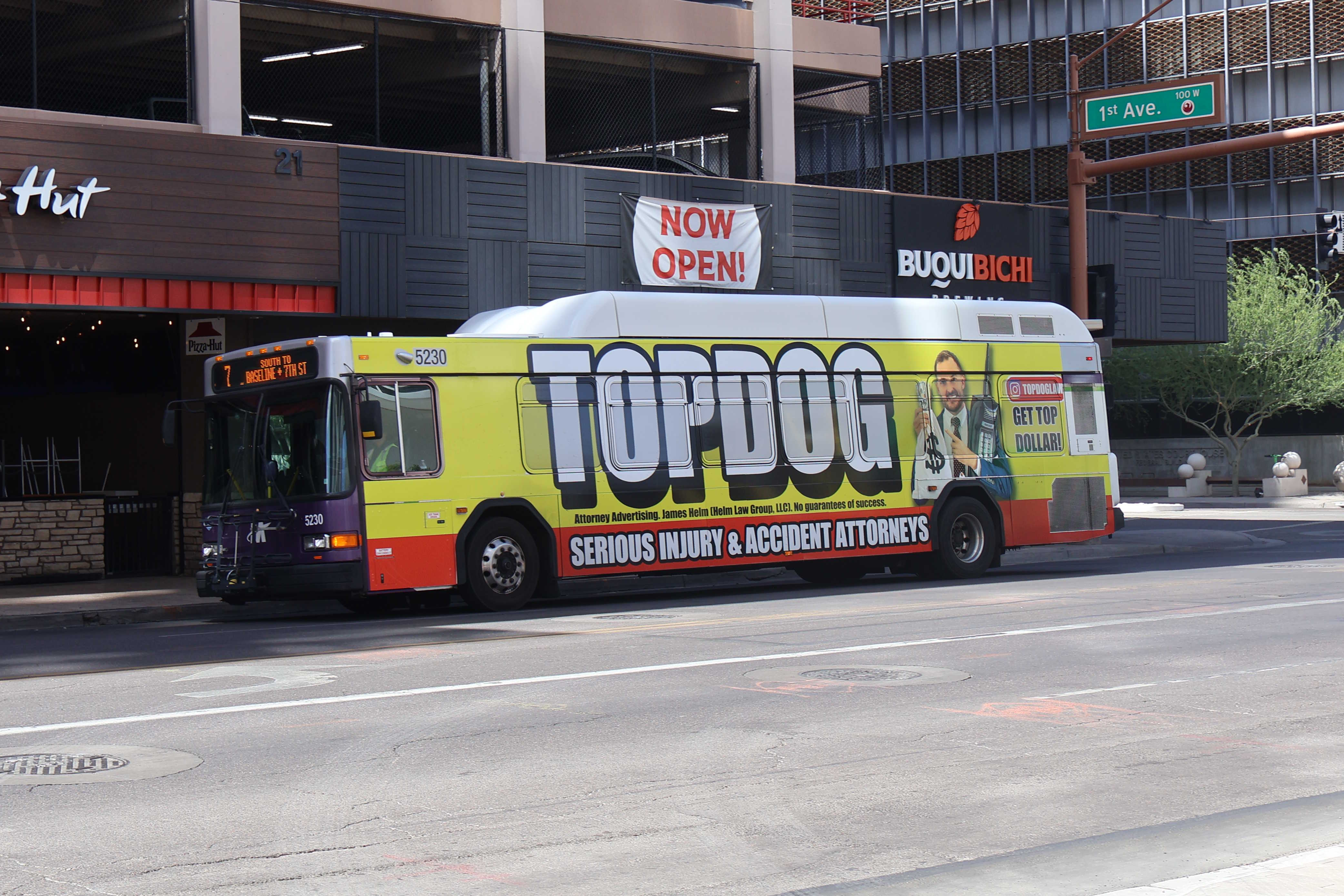 A white and gray Valley Metro bus, with purple and green accent colors, number 5230, traveling eastbound on Van Buren Street in Phoenix on route 7 to 7th Street and Baseline Road