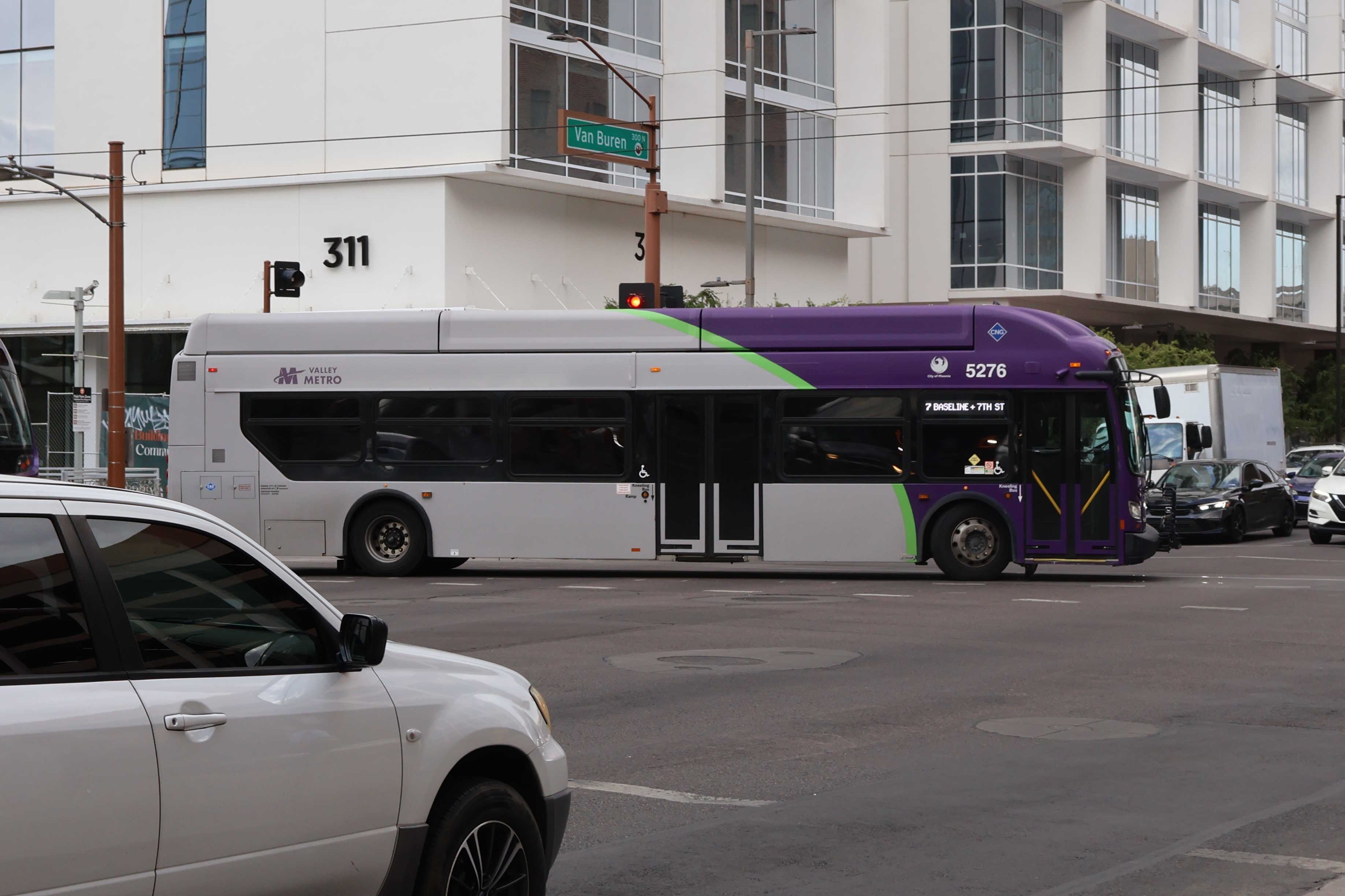 A gray and purple Valley Metro bus, with a green stripe, number 5276, traveling southbound on 1st Avenue in Phoenix on route 7 to 7th Street and Baseline Road